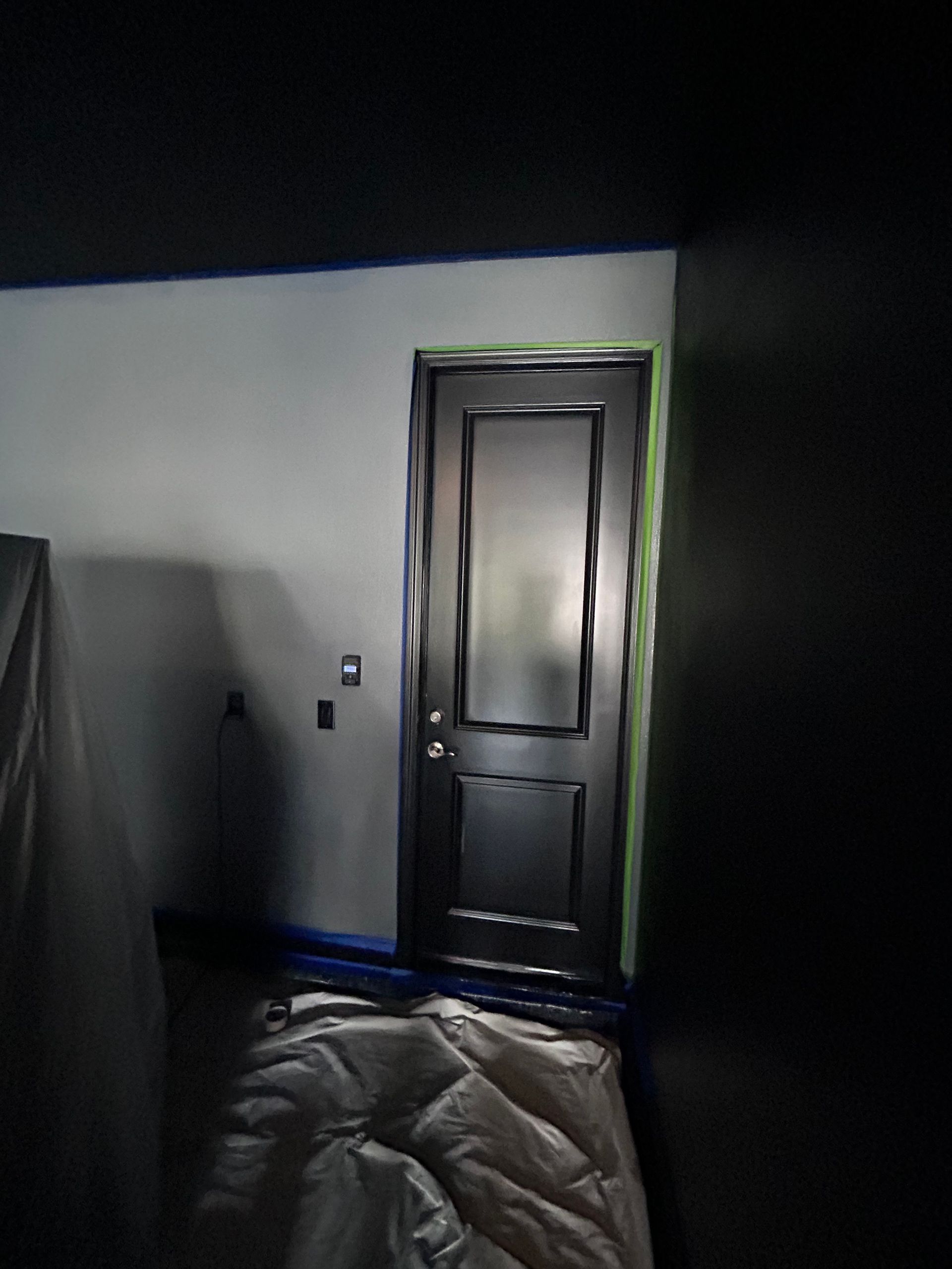 Black door in a room with white and black walls, blue tape, and drop cloths.