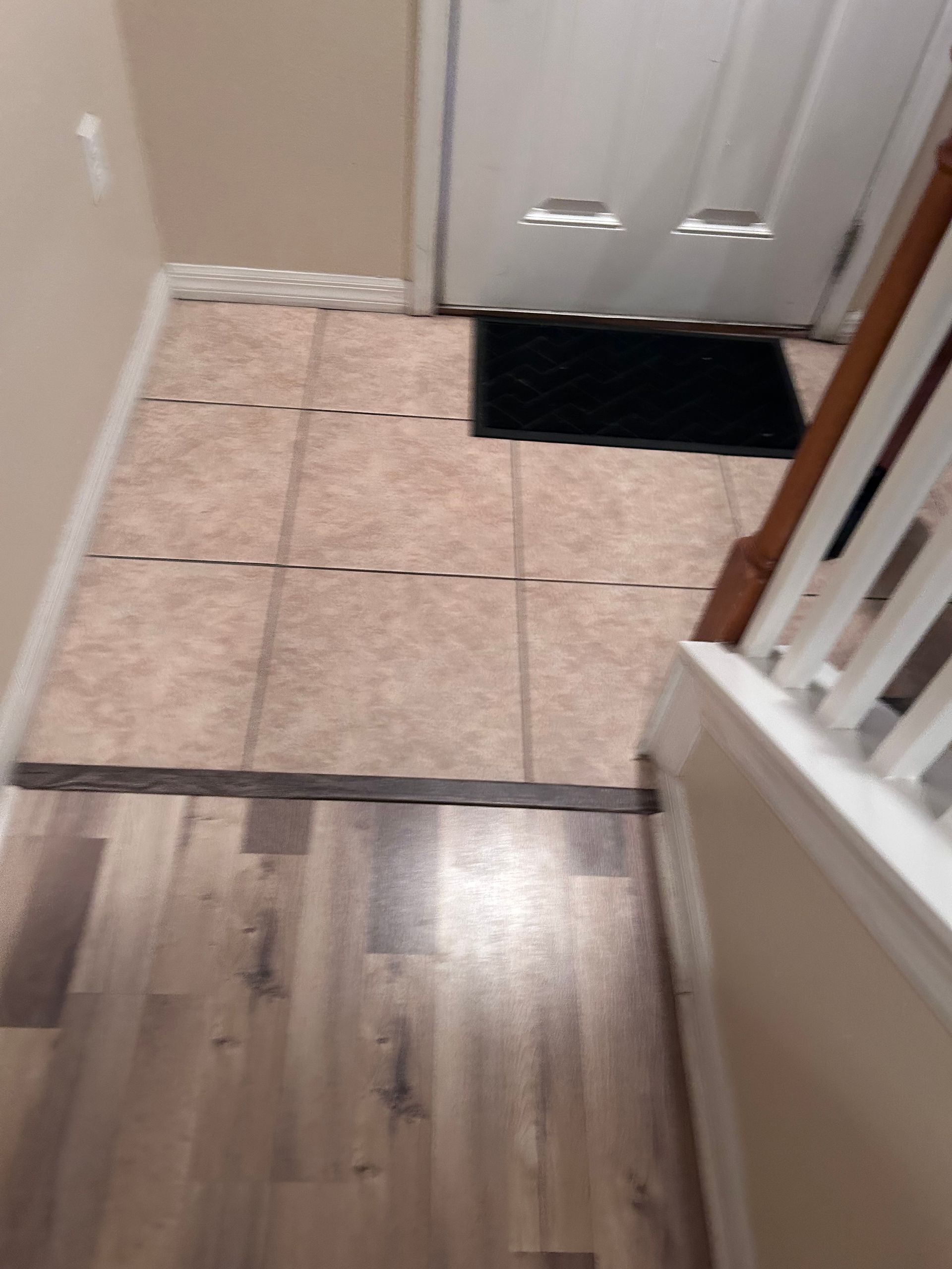 Entryway with tile floor, doormat, wooden flooring, and stairs.
