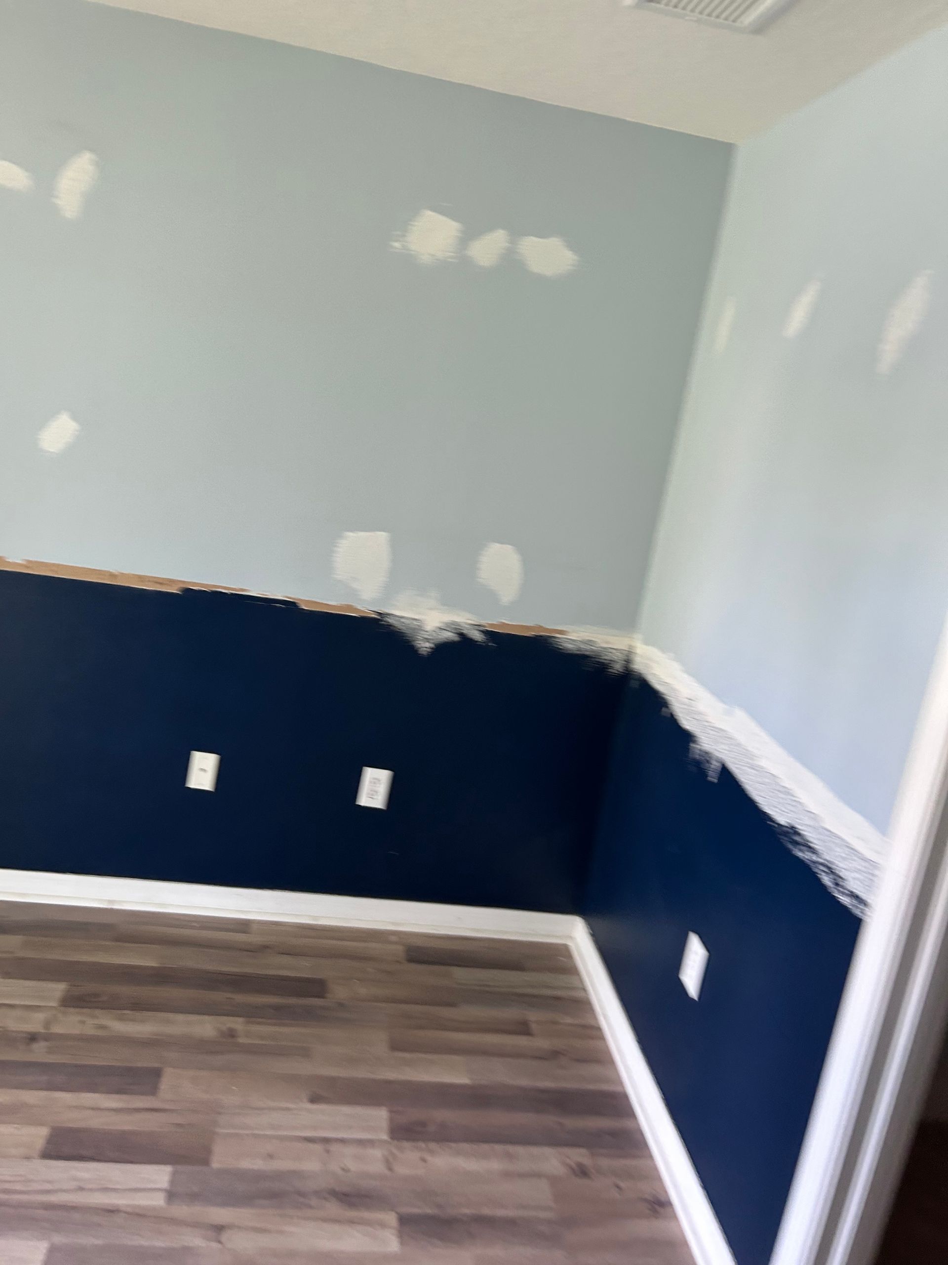 Room with blue and navy walls, white trim, and wood-look flooring. Partially painted, with drywall repair visible.