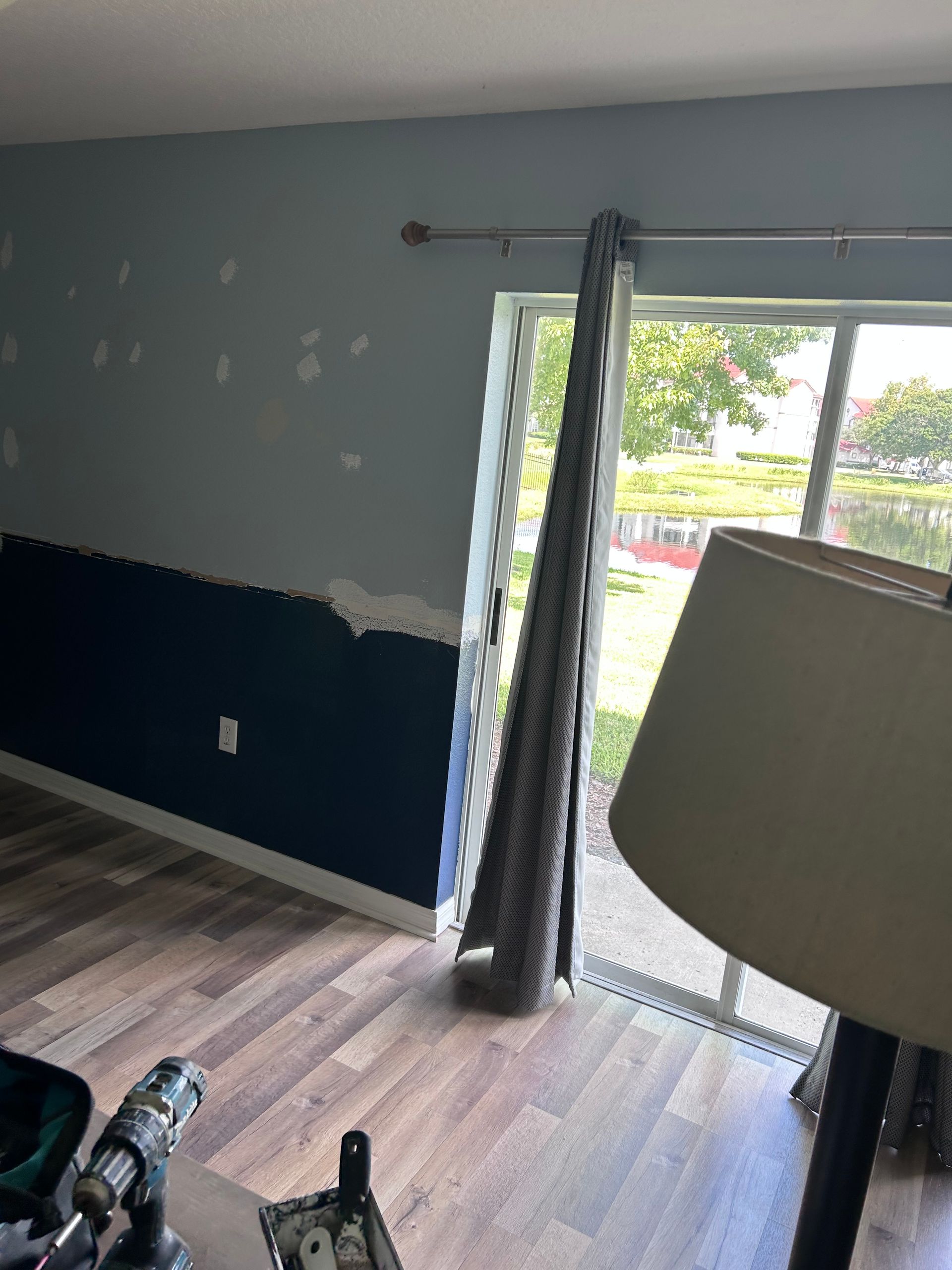 Interior room with blue and dark blue walls, window with drawn curtain, lamp, wood floor.