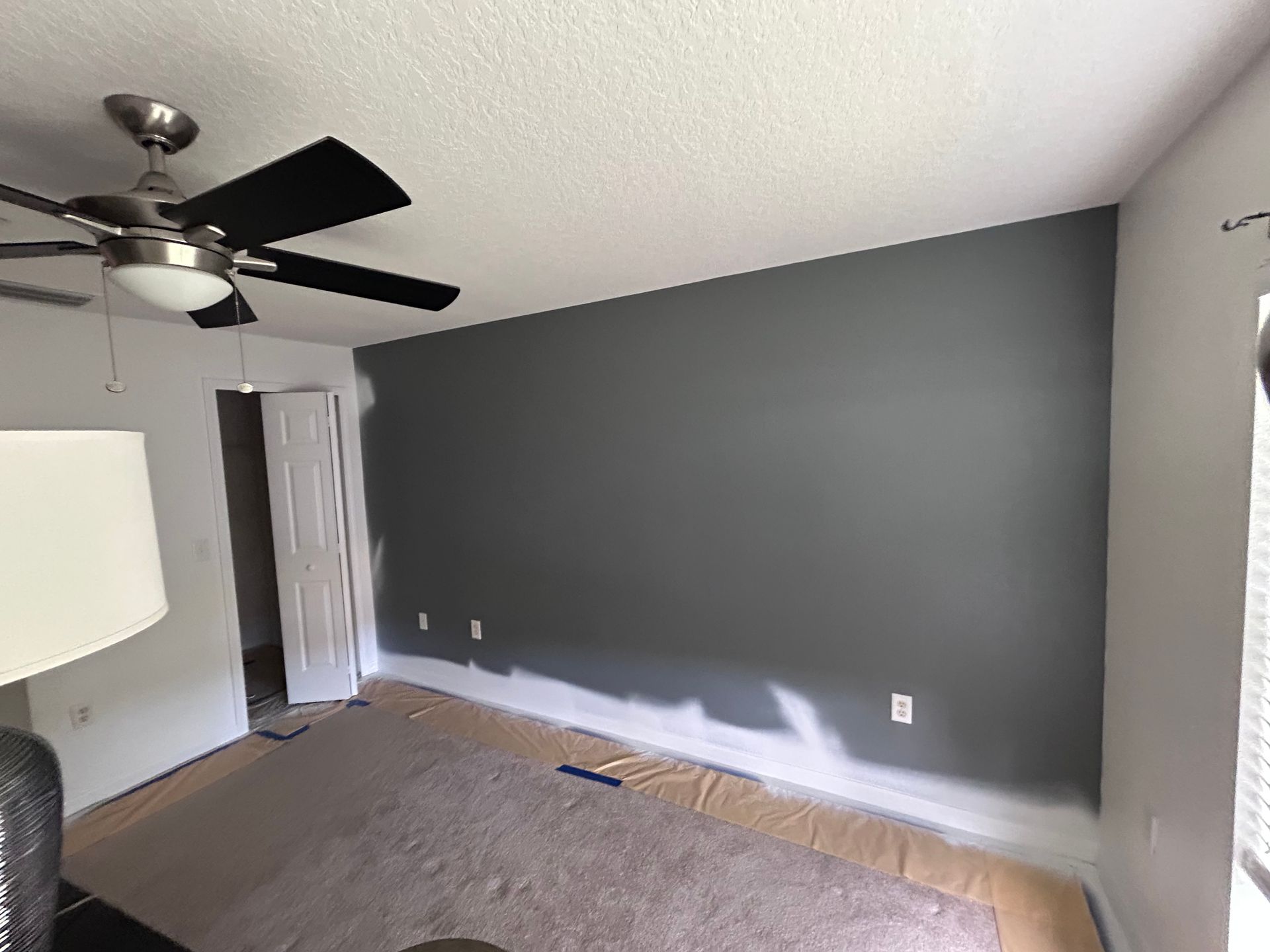Bedroom with a gray accent wall, ceiling fan, and partially painted walls.