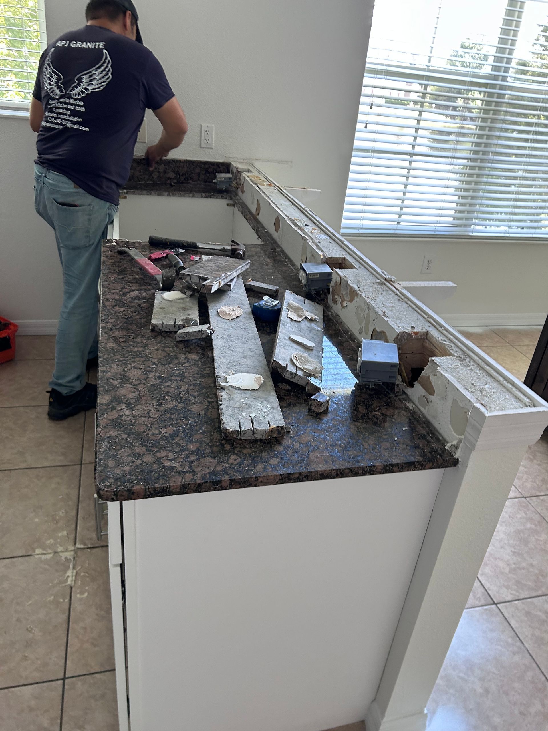Person working on a countertop. Granite countertop with debris. White cabinet and window in background.