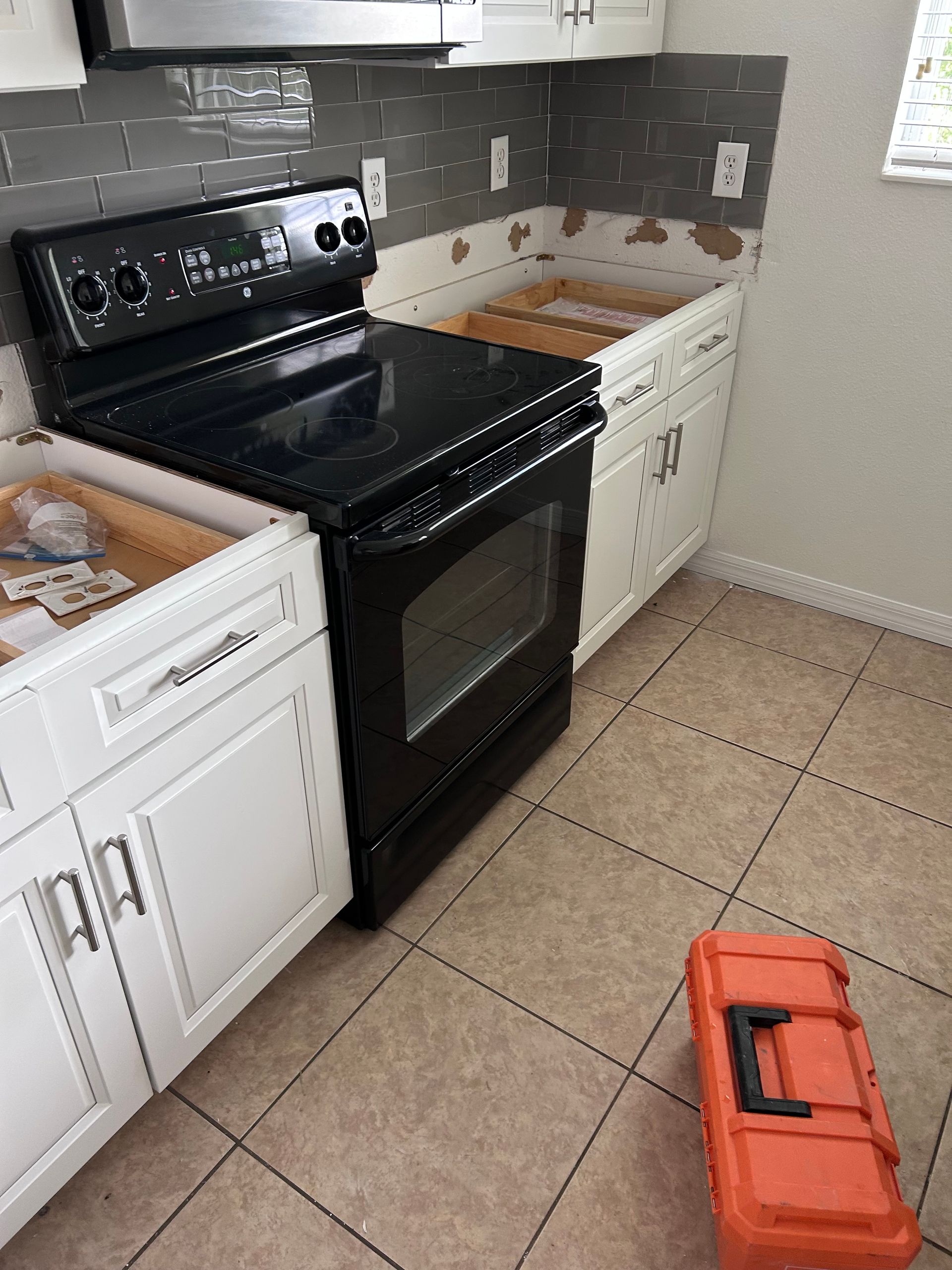 Kitchen under renovation with a black stove and white cabinets; tools on the floor.