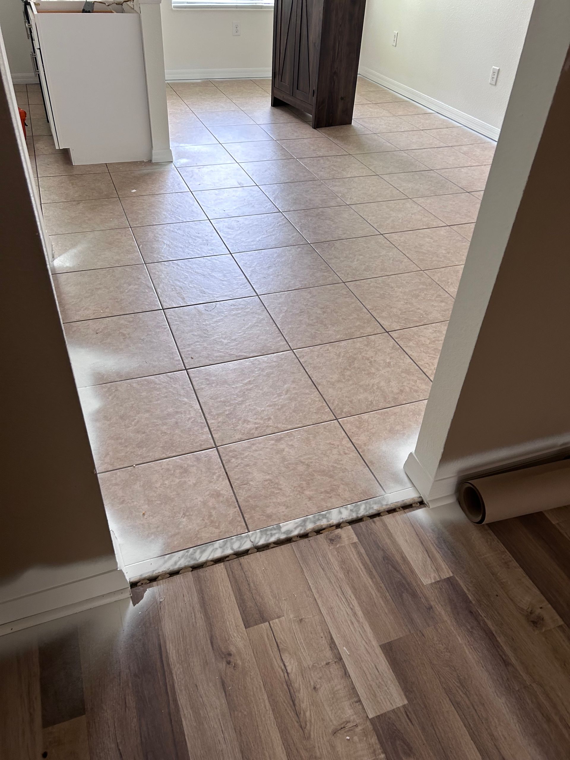 Flooring installation: new wood-look planks in foreground, cork tiles in doorway leading to another room.