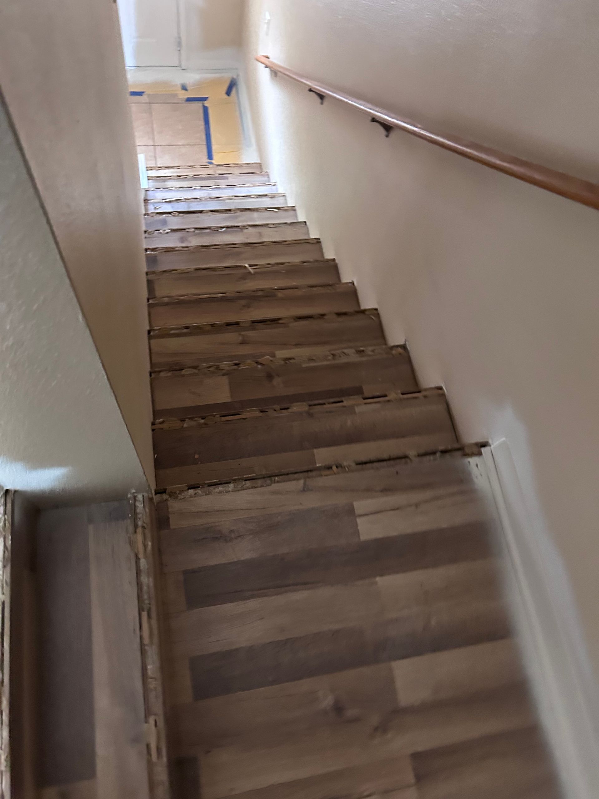 Staircase with wood-look flooring and a wooden handrail on a beige wall, leading upwards.