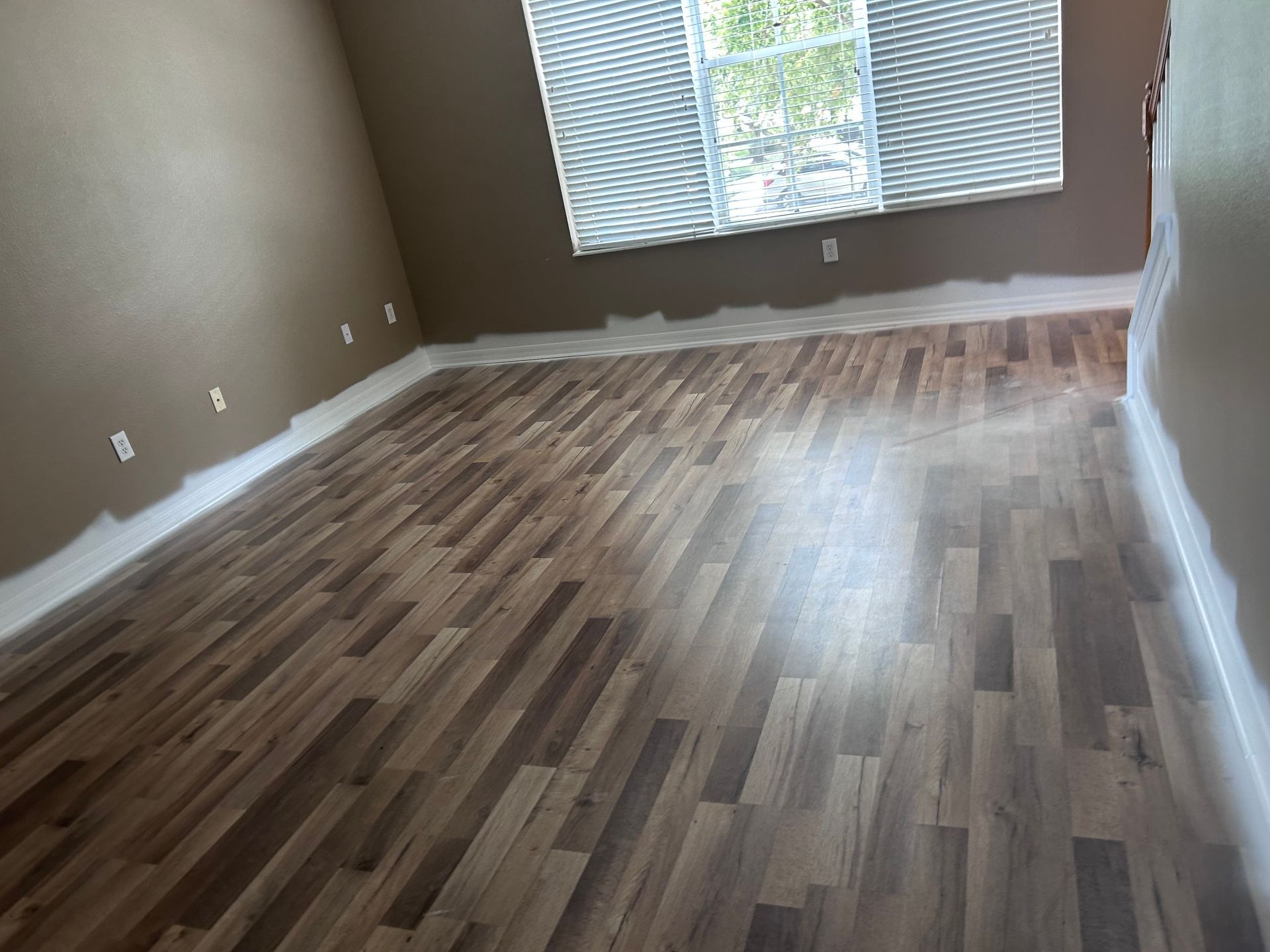 Empty room with brown walls and wood-look flooring, window with blinds.