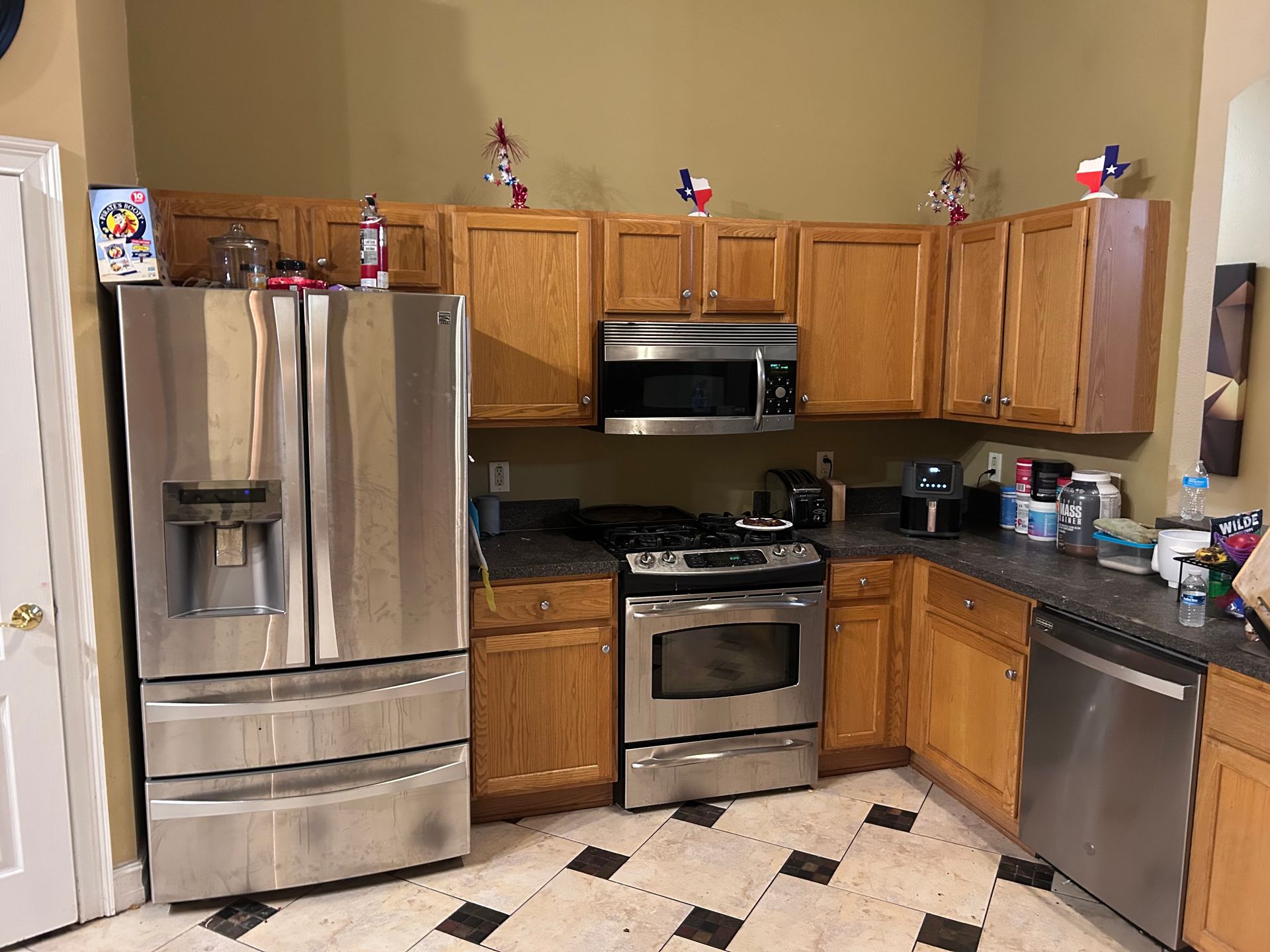 Kitchen with stainless steel appliances, oak cabinets, dark countertops, and tile floor; Texas decorations on upper cabinets.