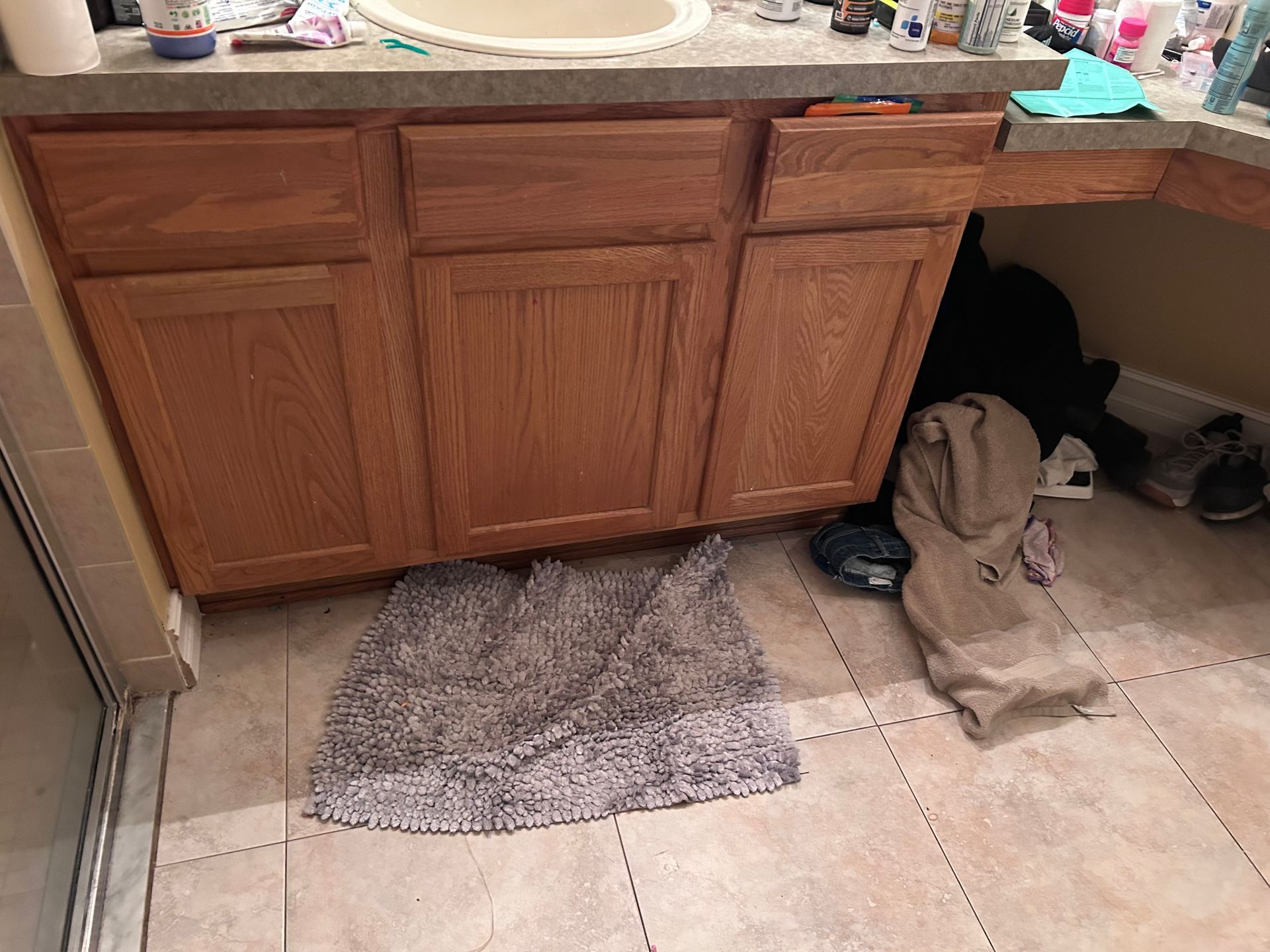 Bathroom vanity with oak cabinets, sink, and a gray bath mat on the floor.