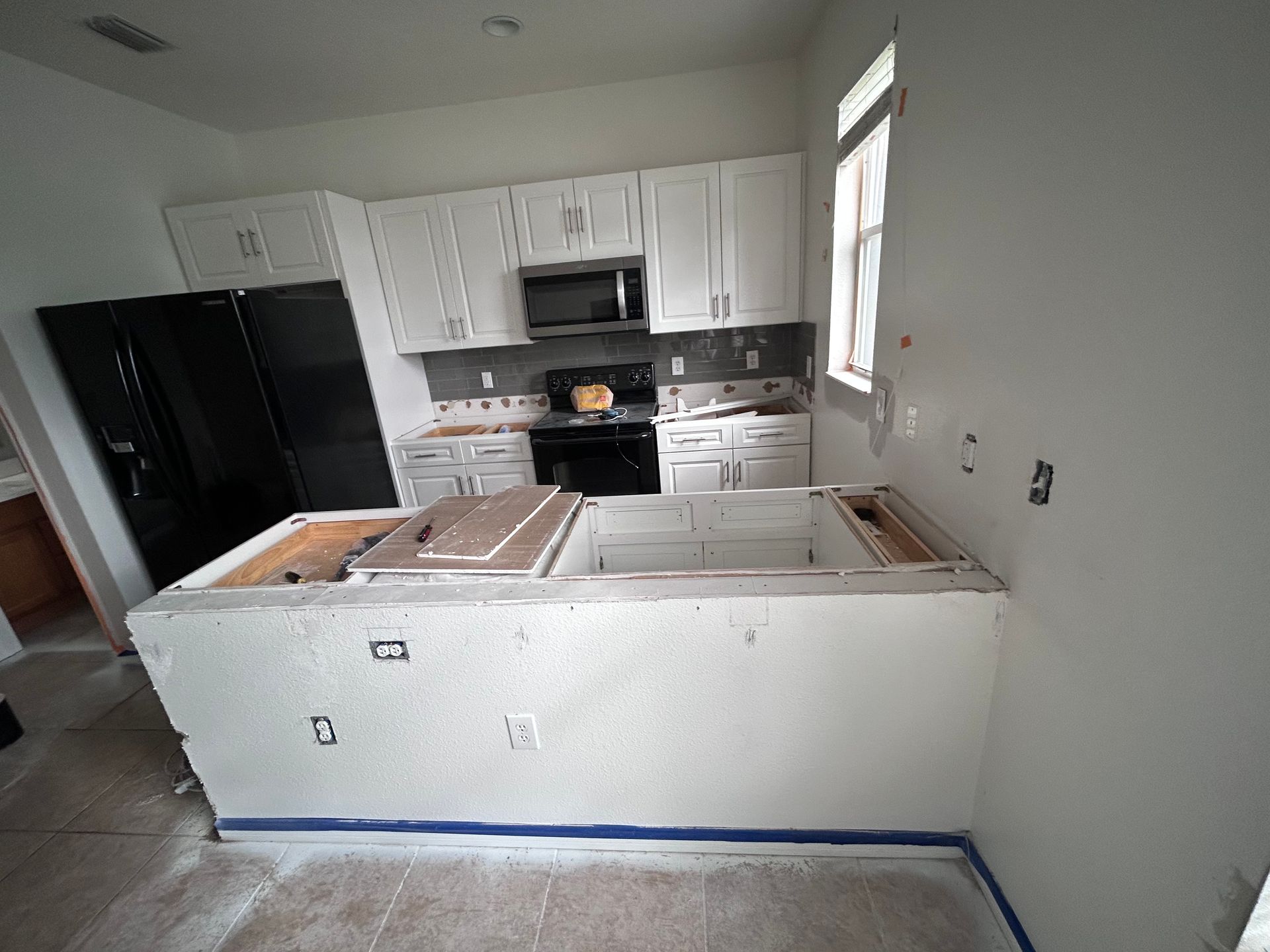 Kitchen undergoing renovation with white cabinets, island, black appliances.