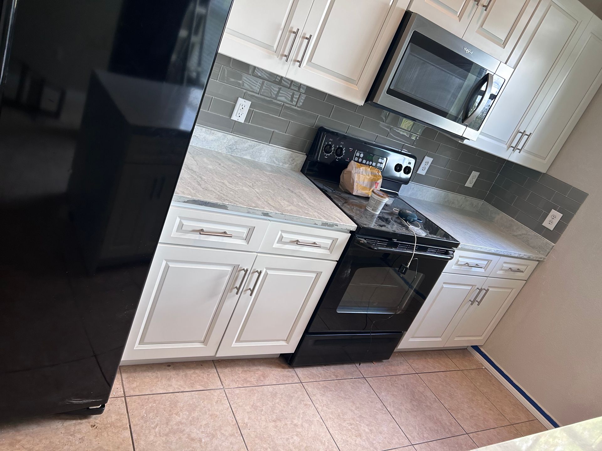 Kitchen with white cabinets, black appliances, gray backsplash, and light countertops.