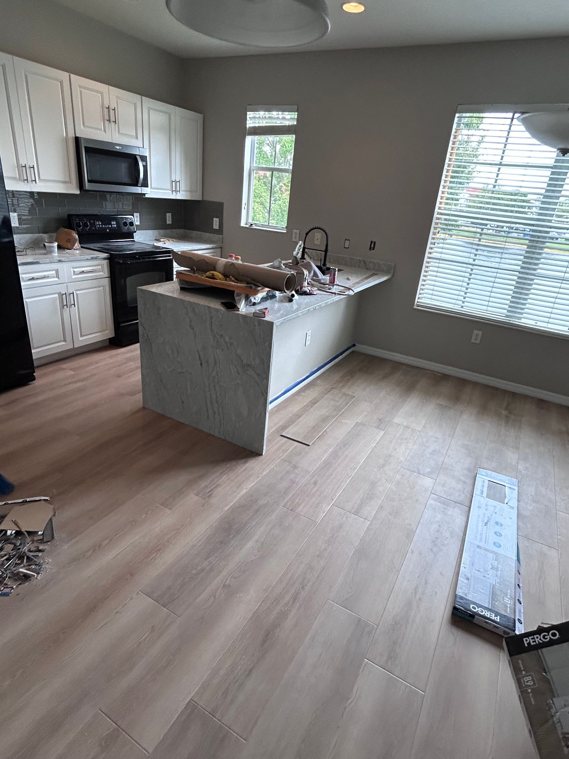 Kitchen with white cabinets, gray backsplash, island, light wood-look flooring, and natural light from window.