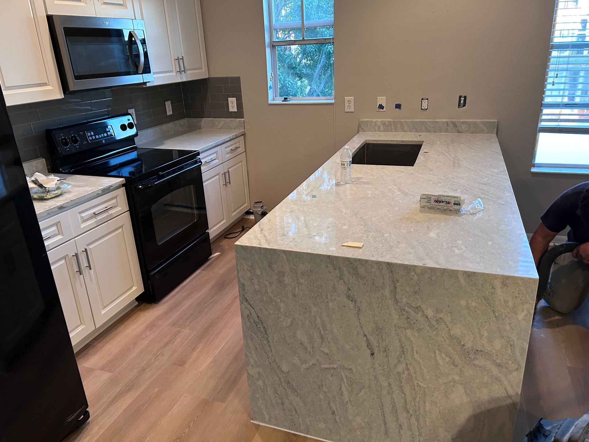 Kitchen with light granite countertops and black appliances; a person works at the island.