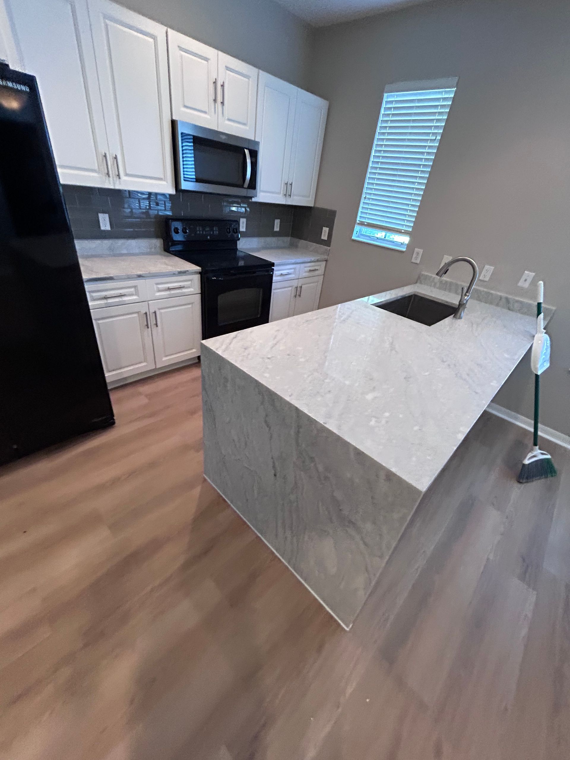Kitchen with white cabinets, black appliances, and a light gray island.