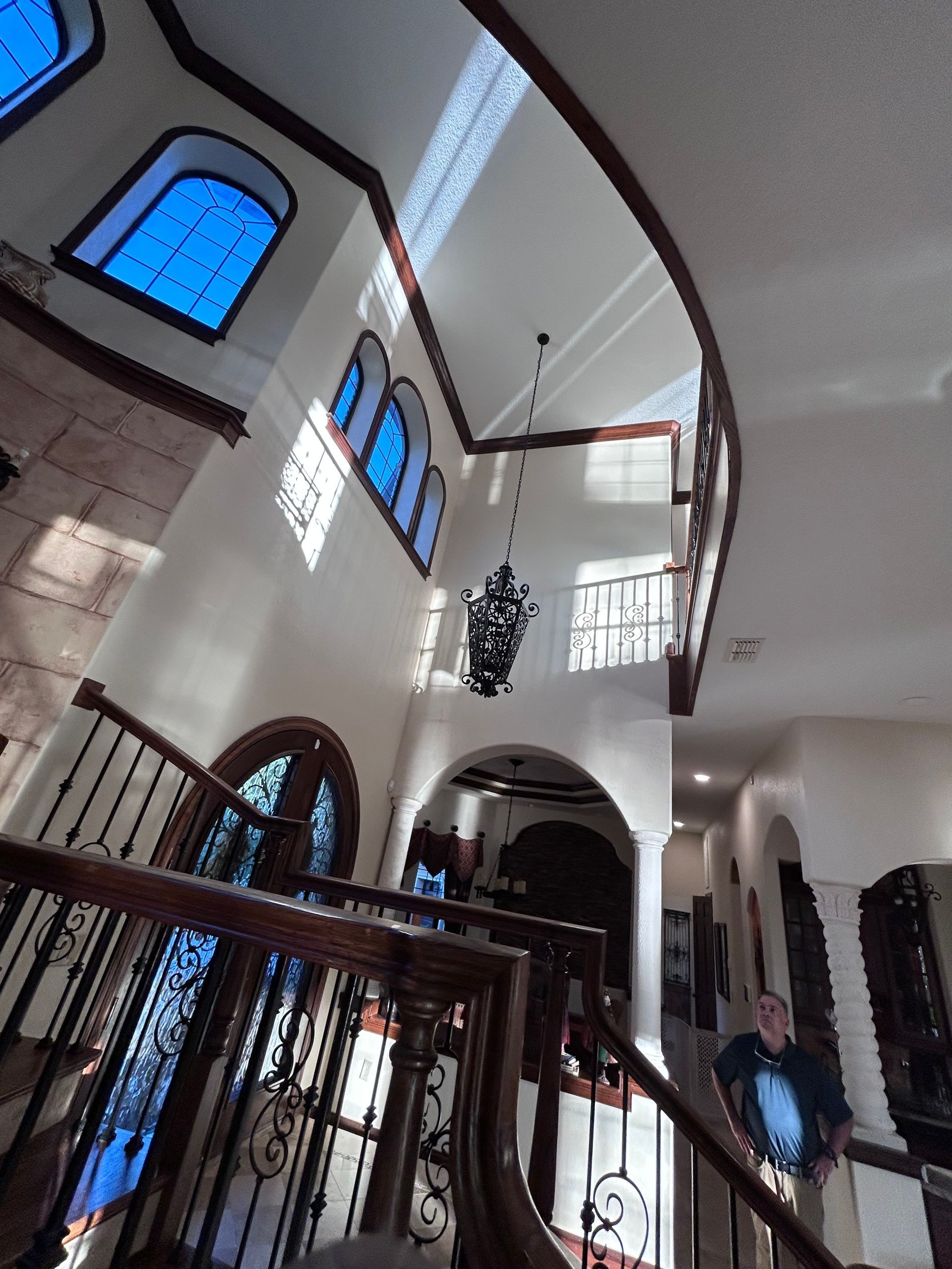 Grand staircase in a multi-story home with blue stained glass windows and a chandelier.