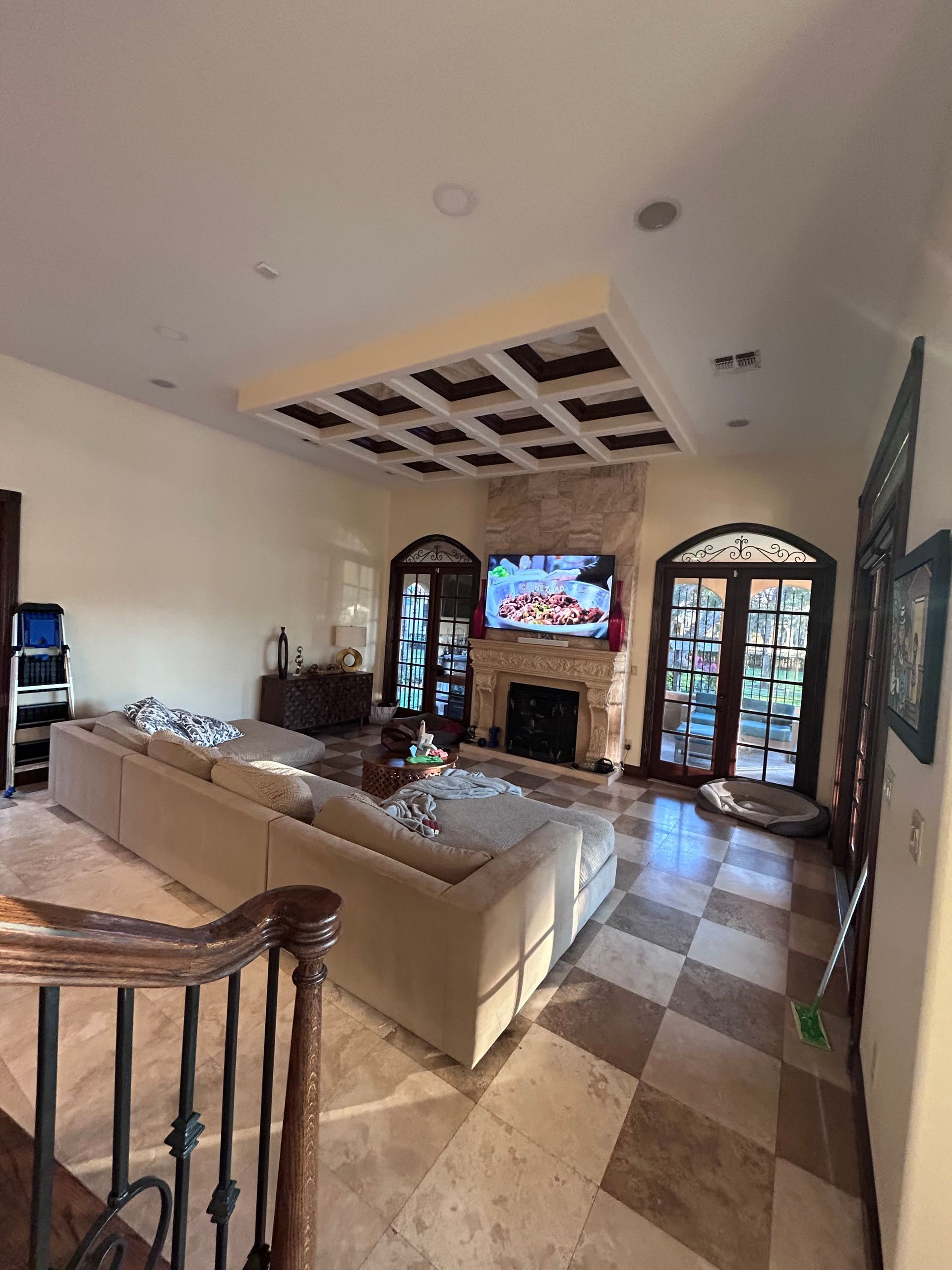 Spacious living room with tan sectional sofa, fireplace, coffered ceiling, and checkerboard floor.