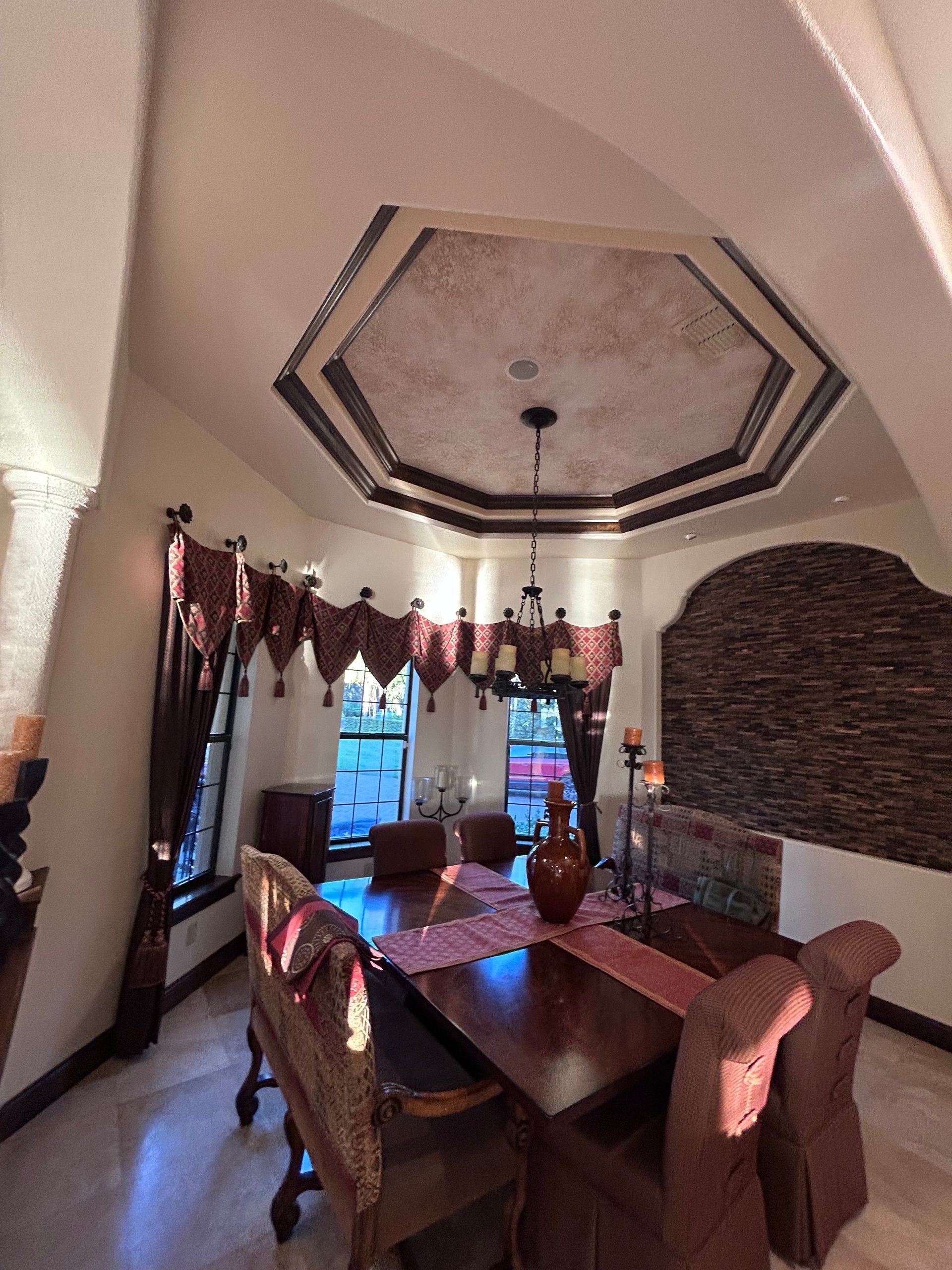 Dining room with ornate ceiling, dark wood table, red runner, and upholstered chairs.