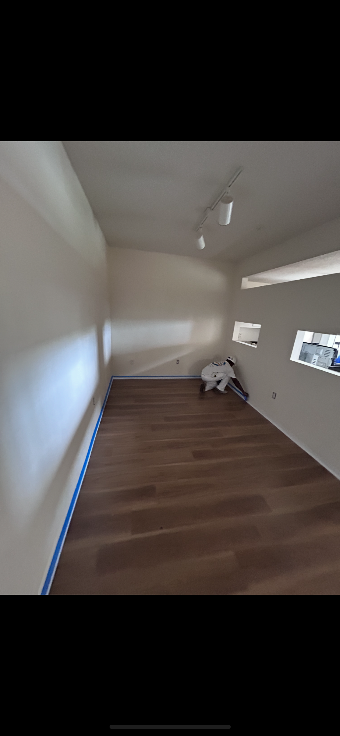 Empty room with wood-like floors, white walls, and recessed display shelves. Track lighting on the ceiling.