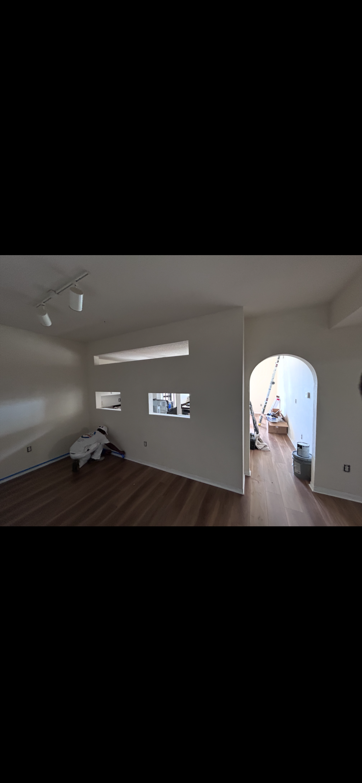 Interior of a room with an arched doorway. Wooden floor and white walls, with light fixtures.