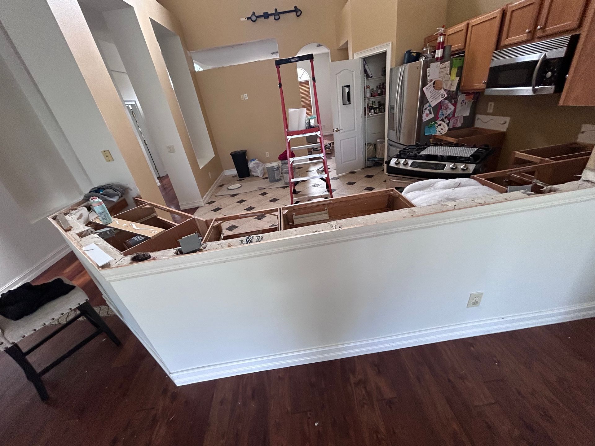 Kitchen renovation in progress: a white half-wall with exposed framework, ladder, appliances, and cabinetry.