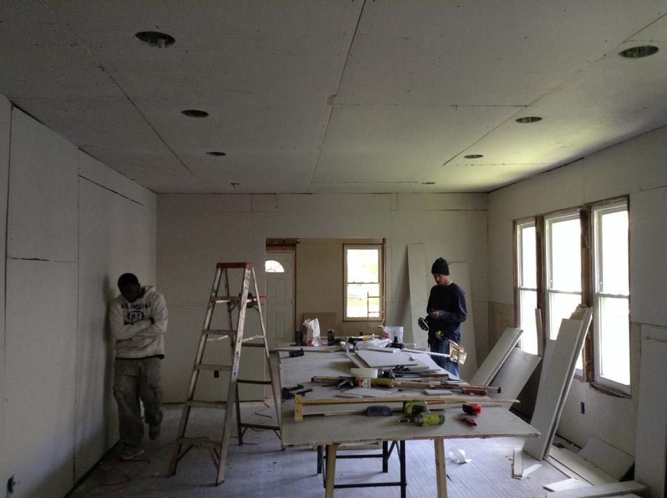 Two men are working in a room with a ladder and a table