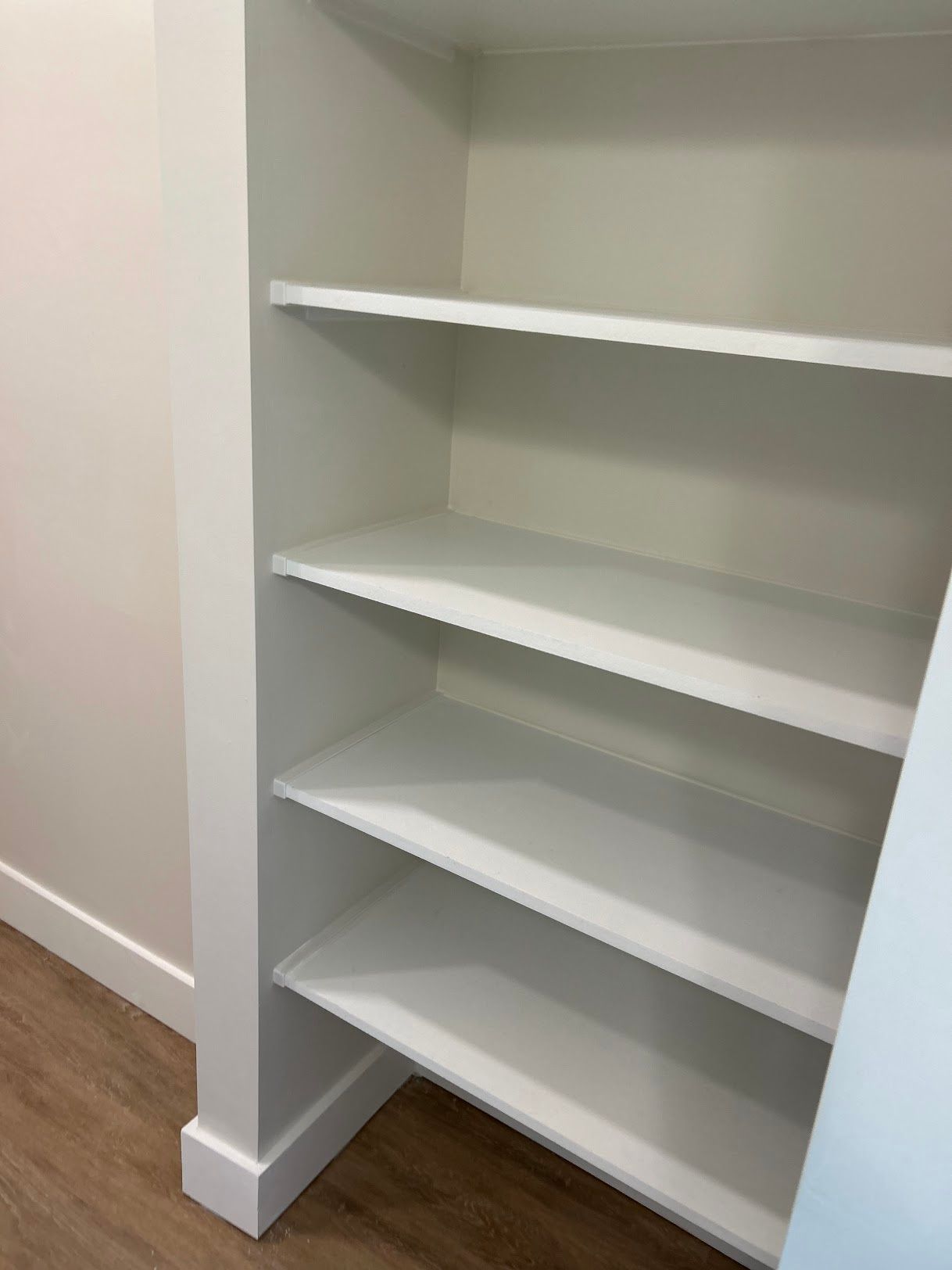 A closet with white shelves and a wooden floor.