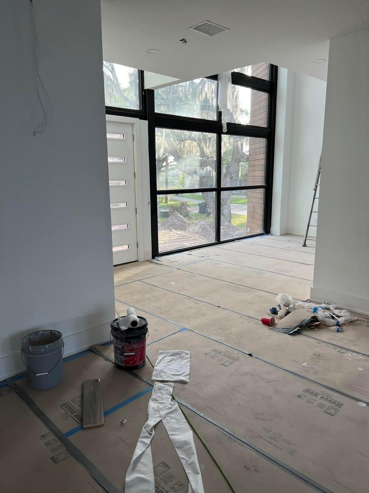A room with a lot of windows and a bucket of paint on the floor.