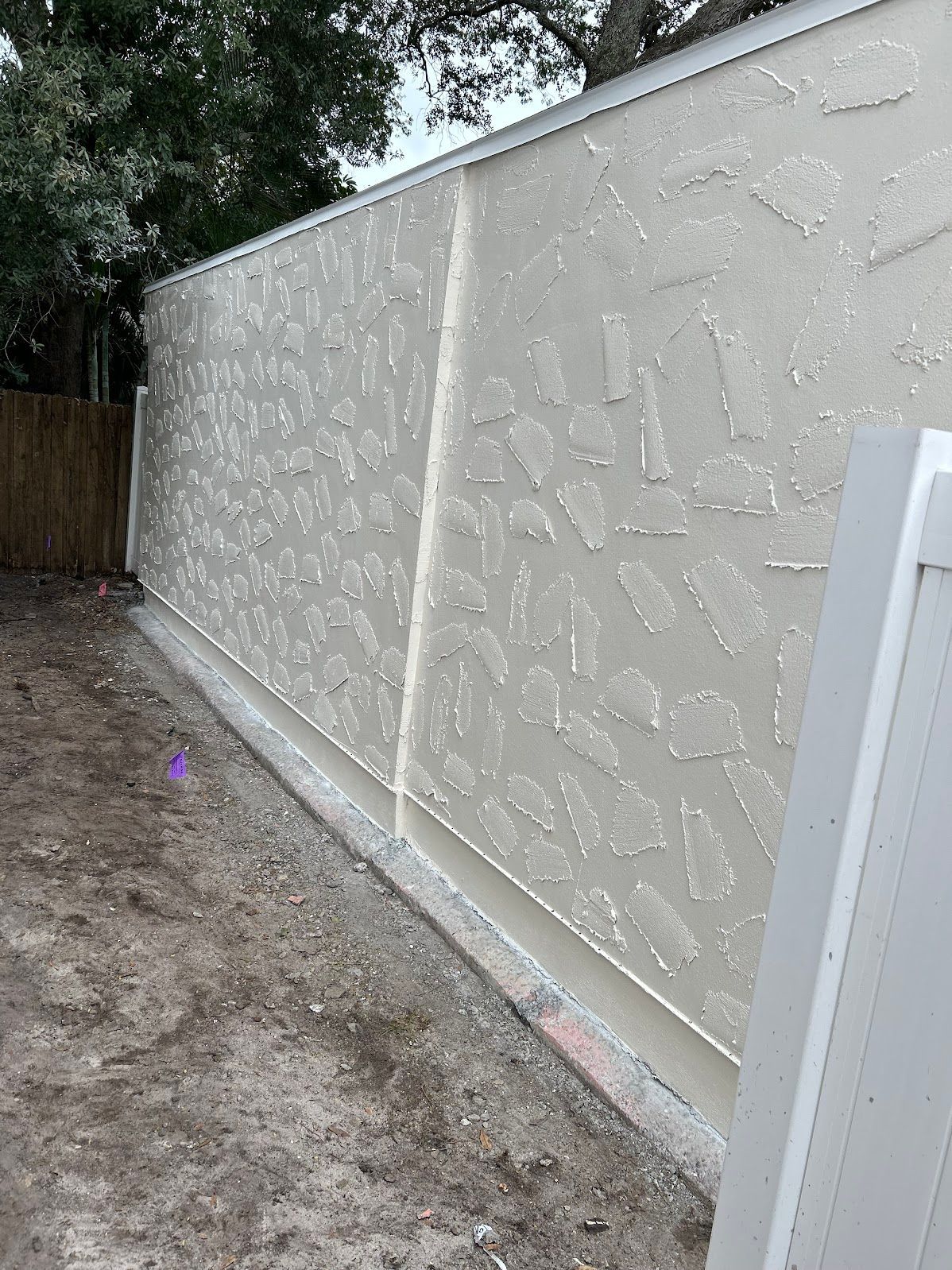 A white fence is surrounded by dirt and trees in a backyard.