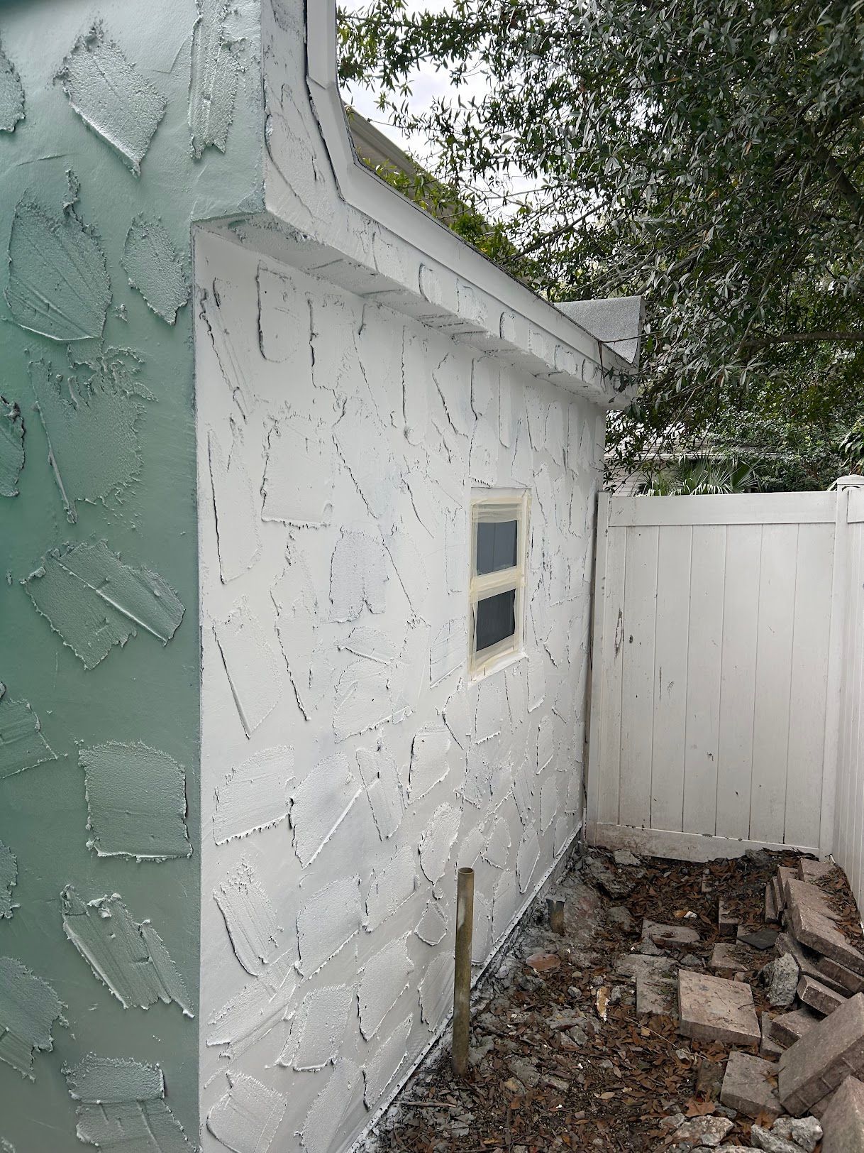 The side of a house with a window and a white fence.