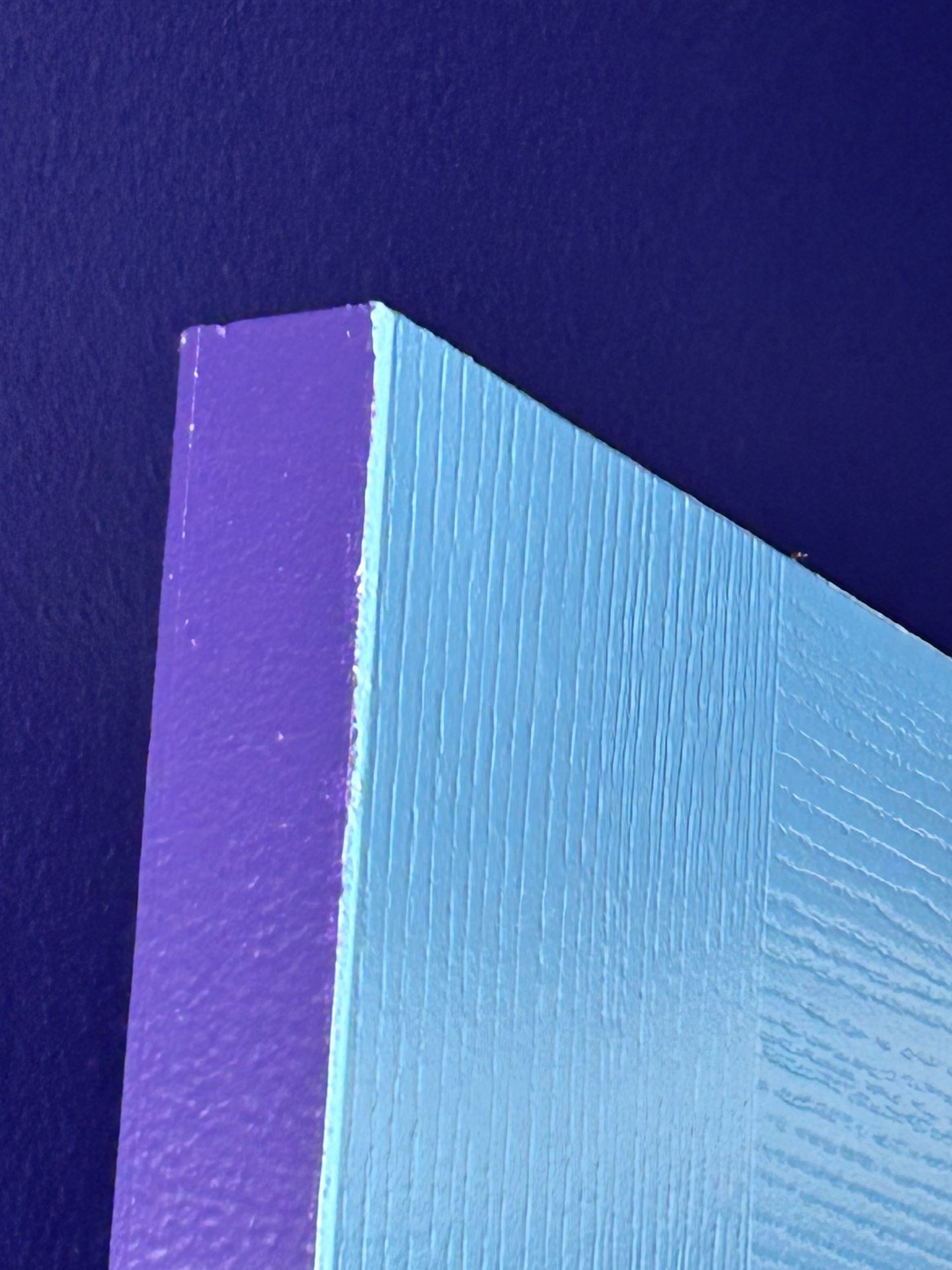 A blue and purple piece of wood against a purple wall