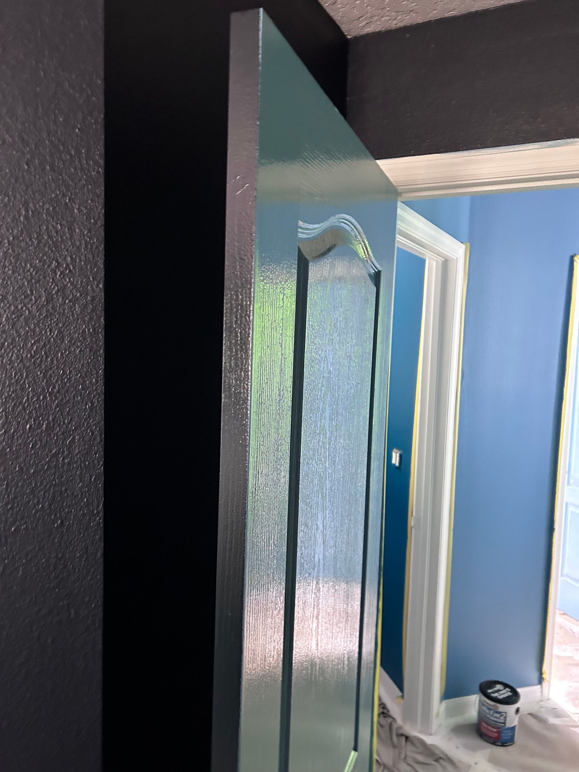 A door is being painted in a room with blue walls