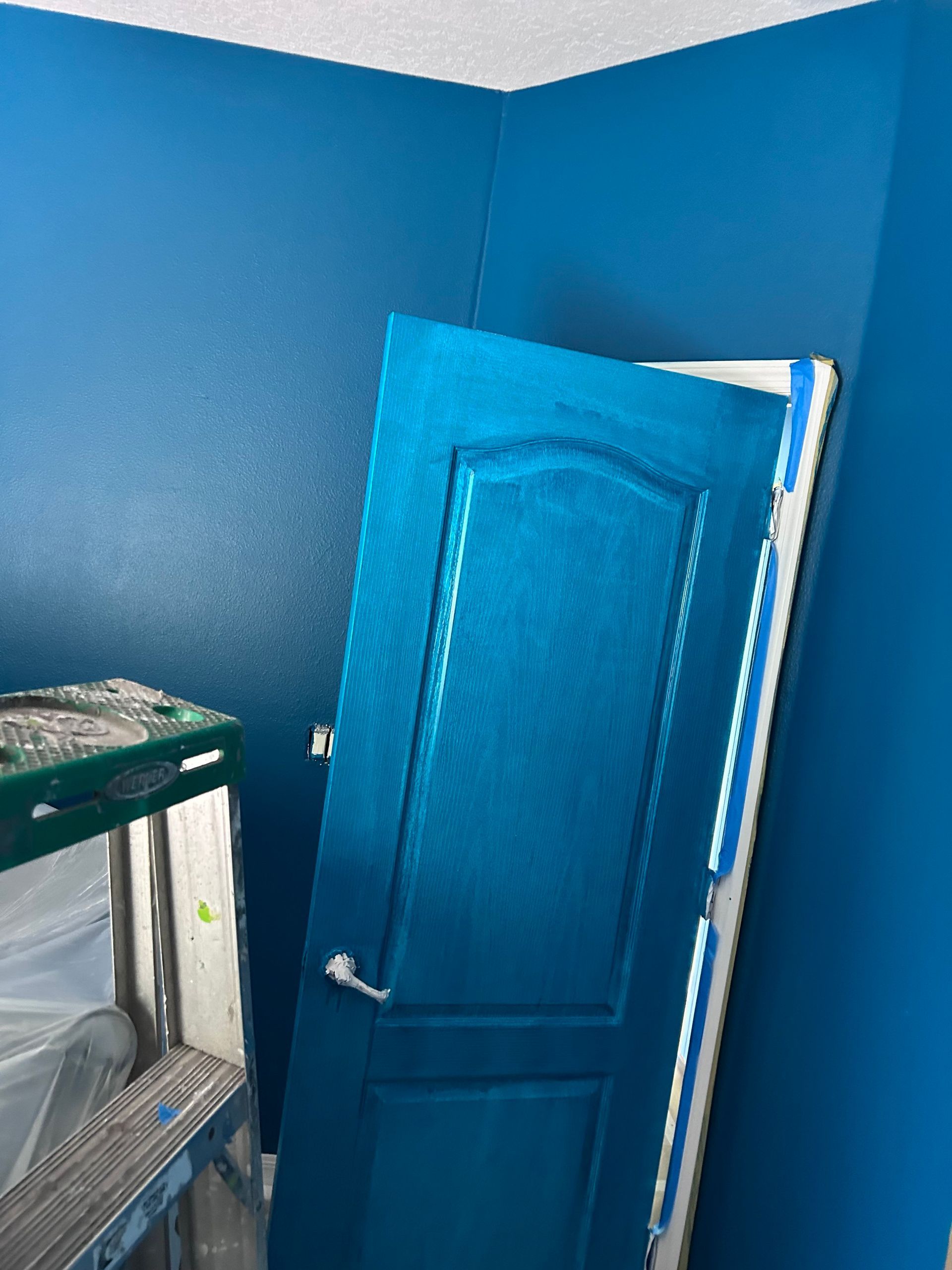 A blue door is being painted in a room with blue walls