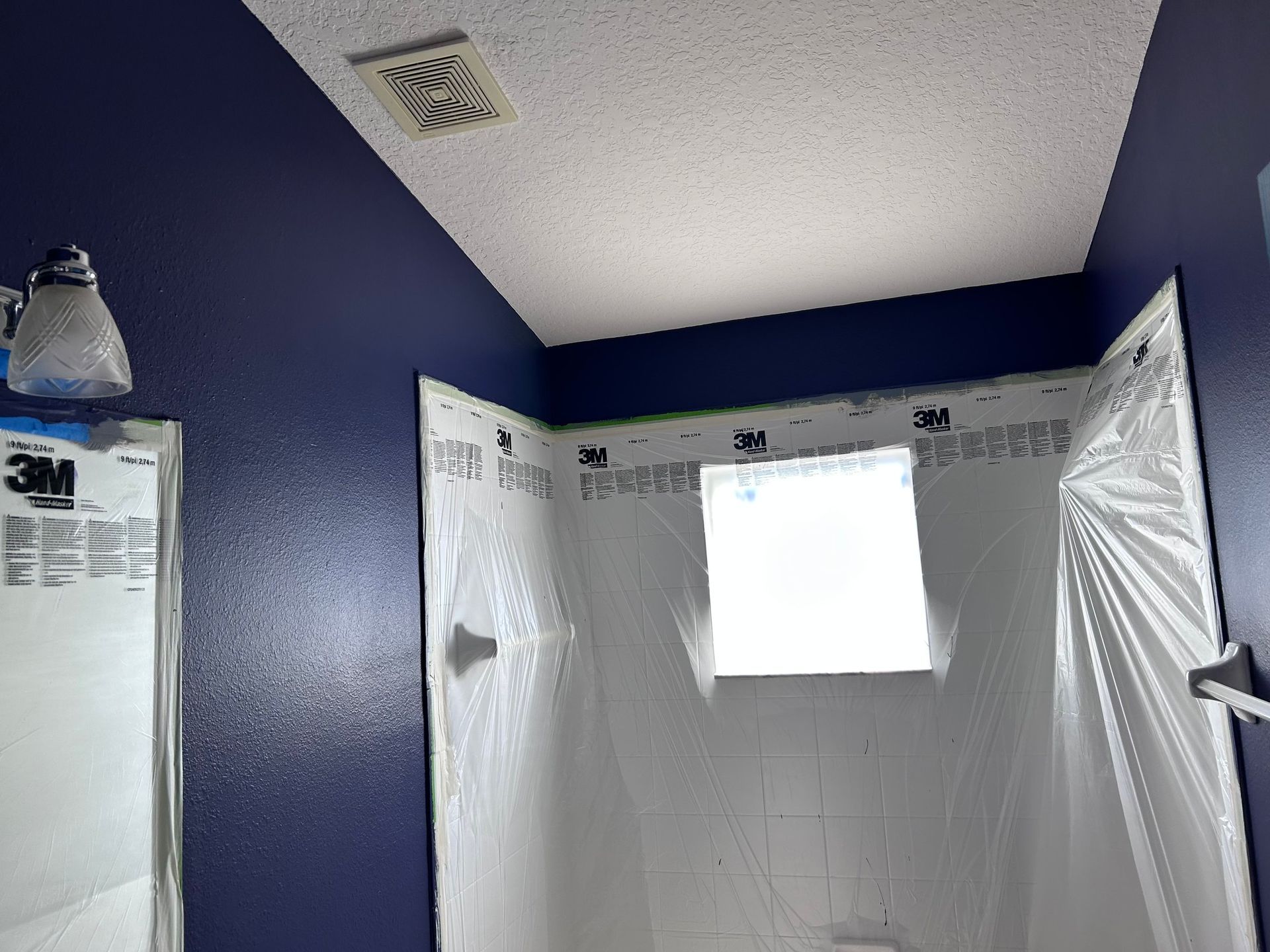 A bathroom with blue walls and white tiles is being painted.