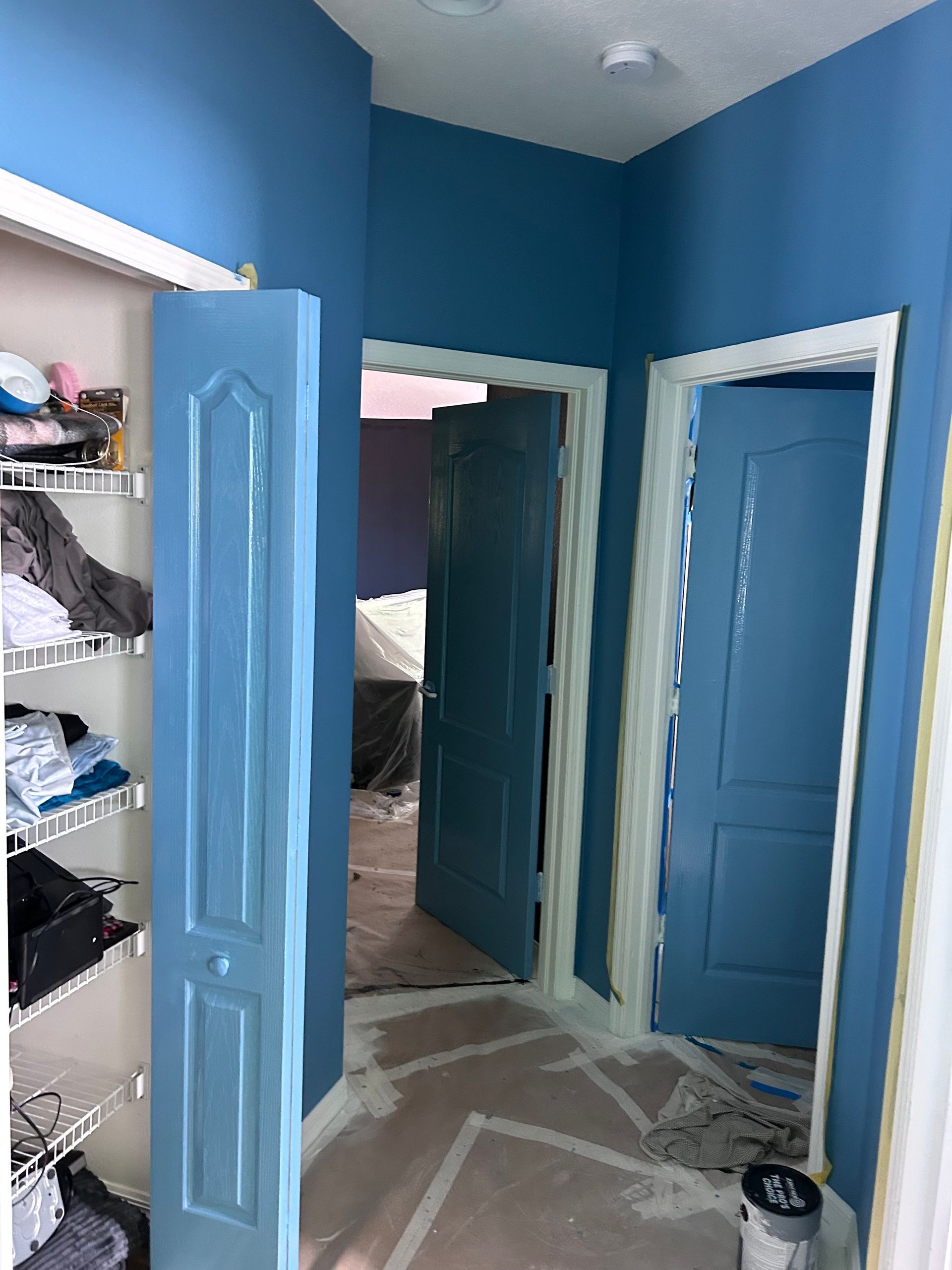 A closet with blue walls and blue doors is being painted.