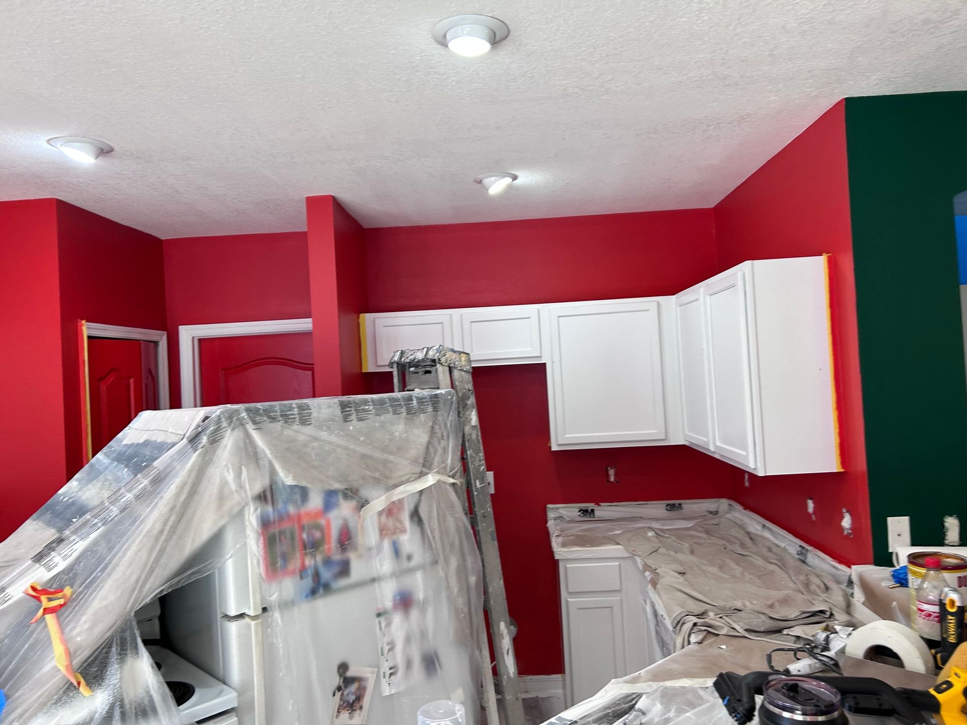 A kitchen with red walls and white cabinets is being painted