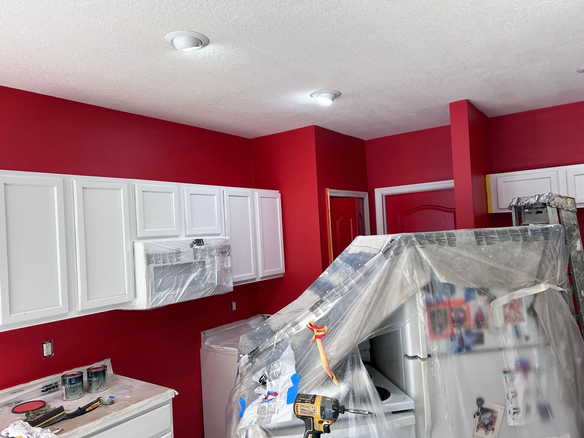 A kitchen with red walls and white cabinets is being painted.