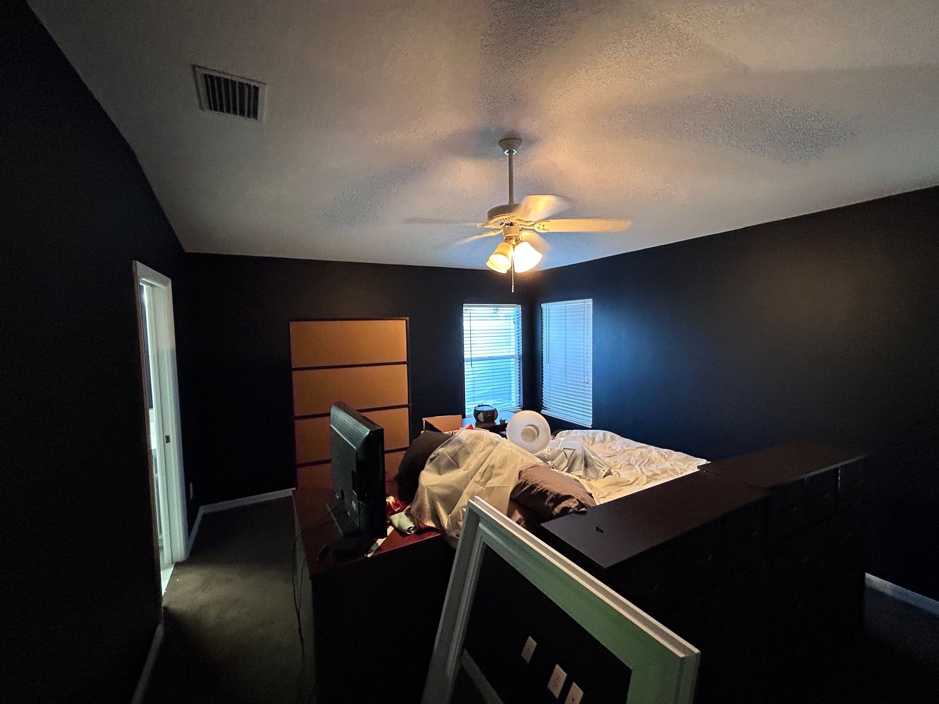 A bedroom with black walls and a ceiling fan.