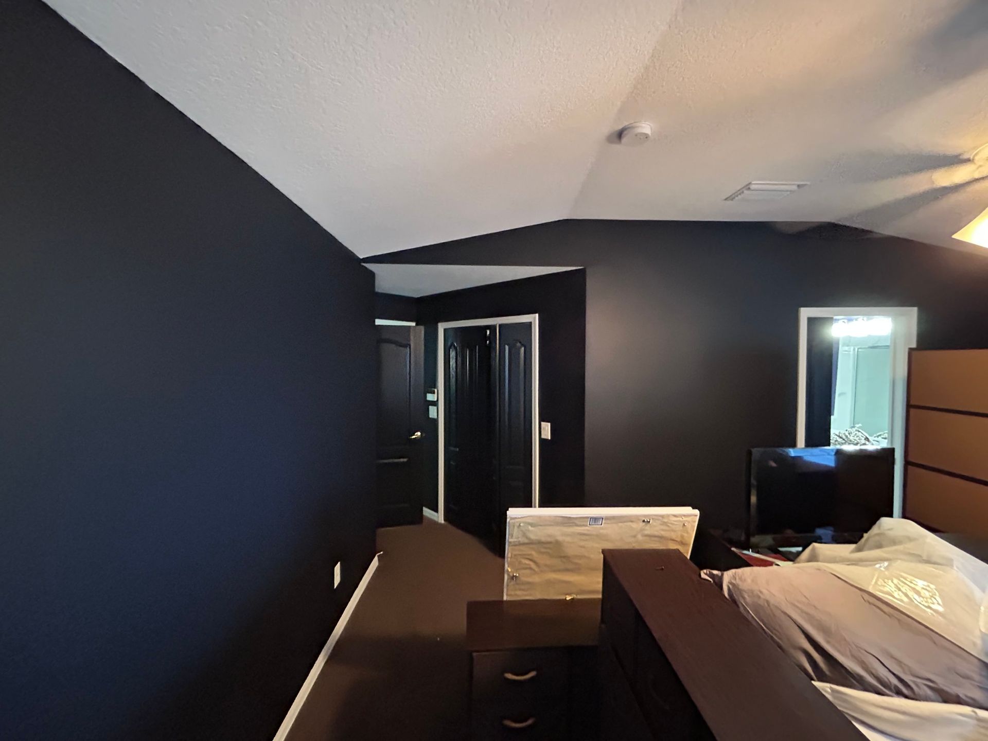 A bedroom with black walls and a bed and a television