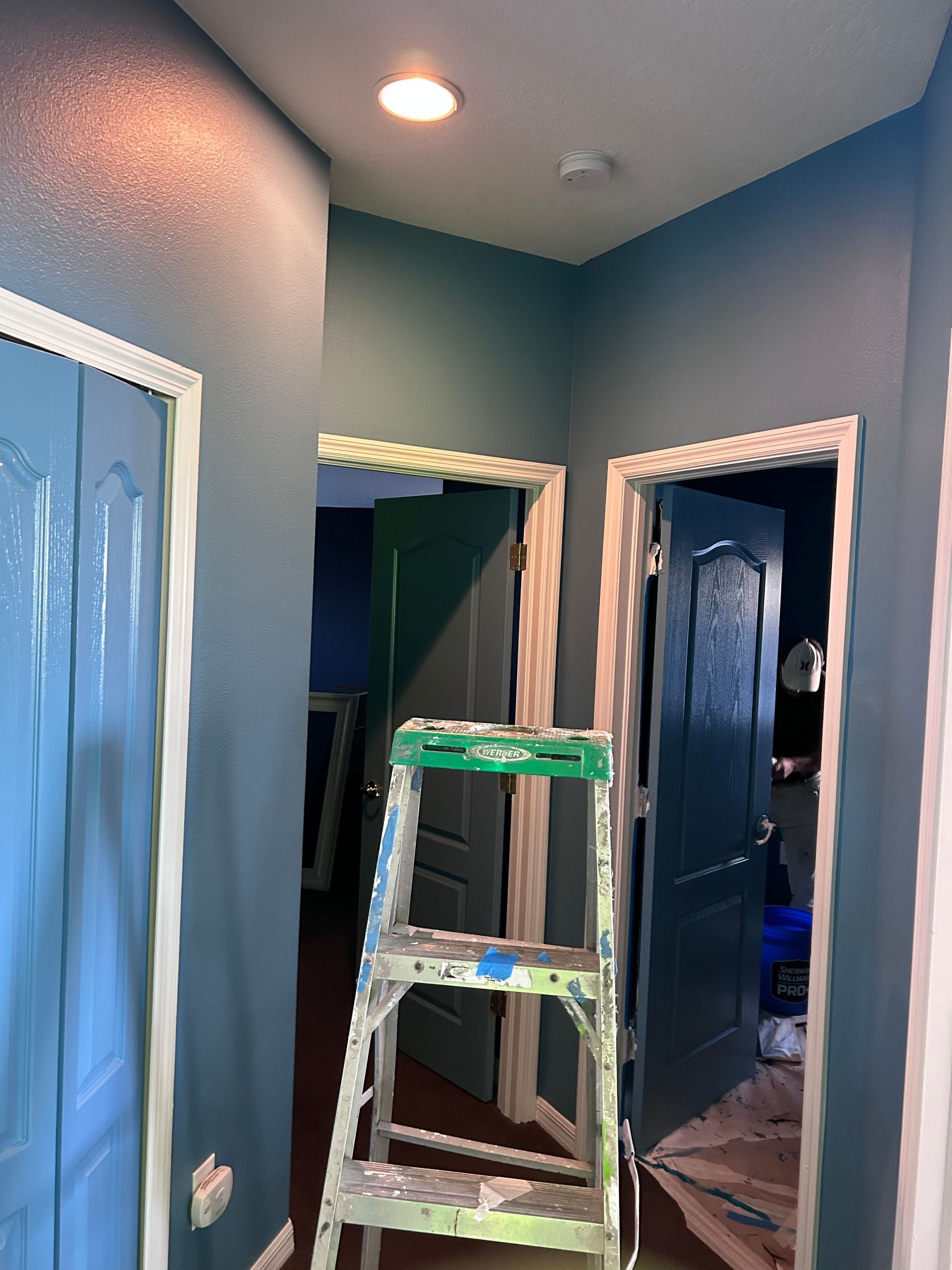 A ladder is sitting in a hallway between two doors.