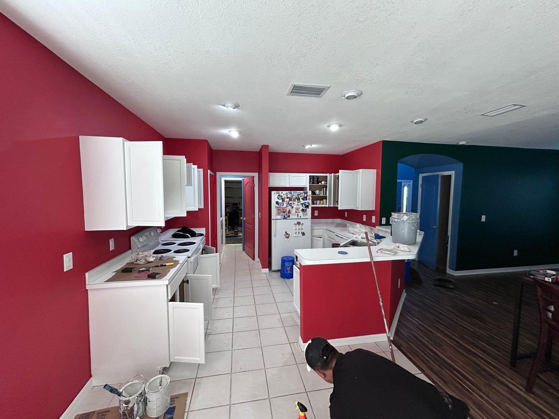 A man is kneeling in a kitchen with red walls and white cabinets