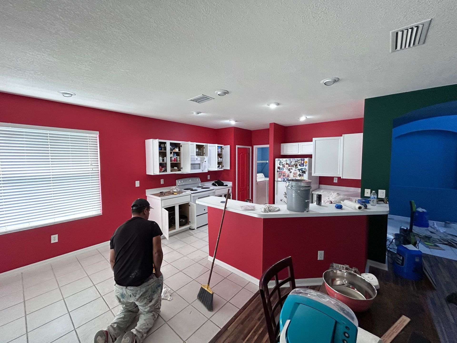 A man is kneeling down in a kitchen with red walls
