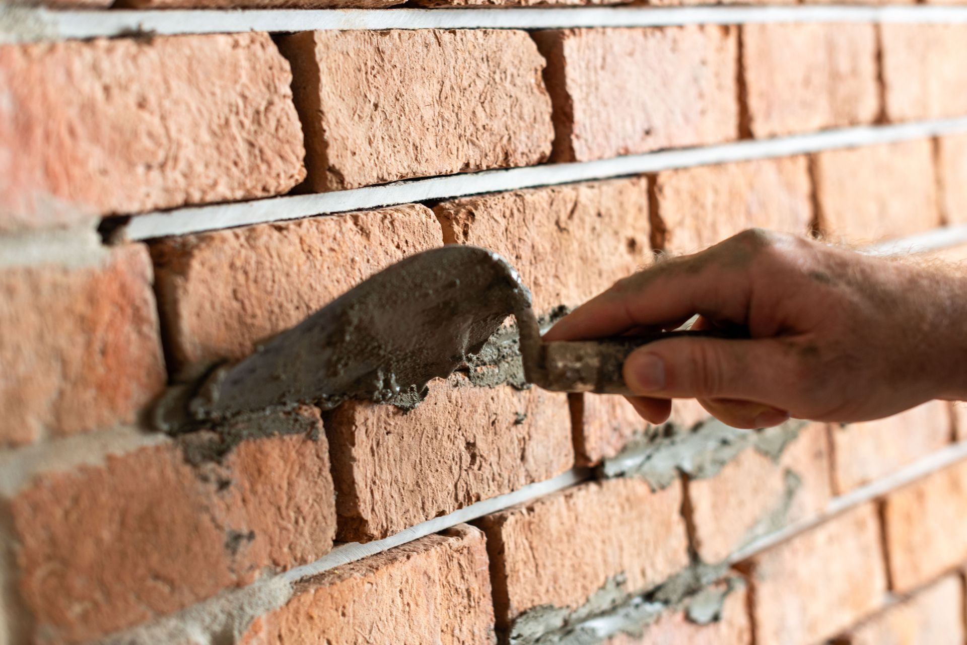 Mason applying mortar between brick courses with trowel
