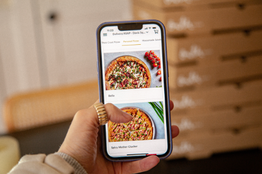 A person is holding a cell phone with a pizza on the screen.