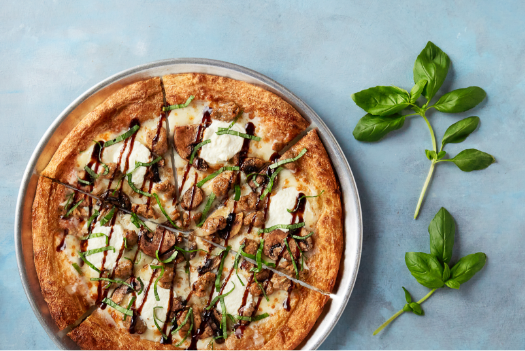 A pizza with basil leaves on a plate on a table.