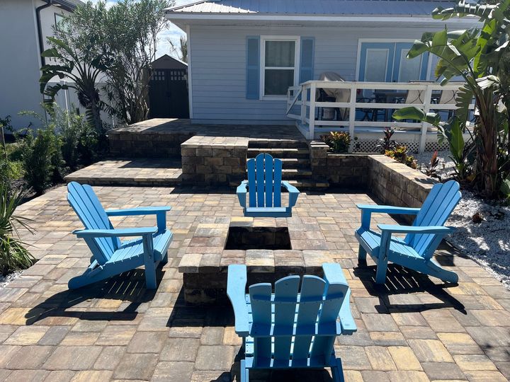 A patio with blue chairs and a fire pit in front of a house.