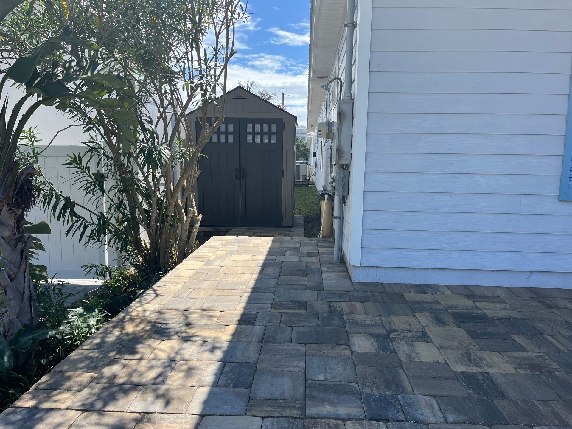 A brick walkway leading to a shed on the side of a house.