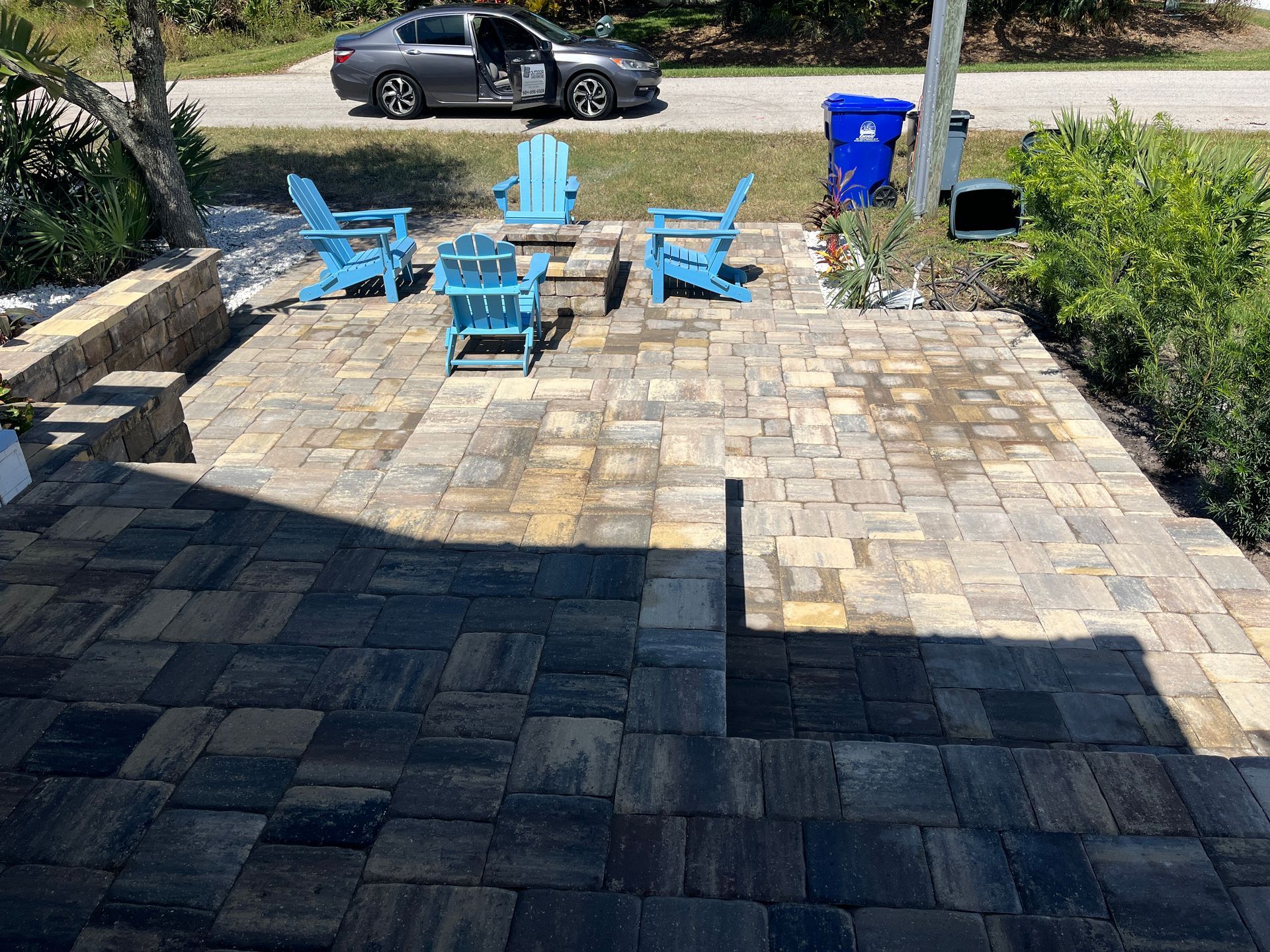 A paver patio with blue chairs and a car parked in the background.