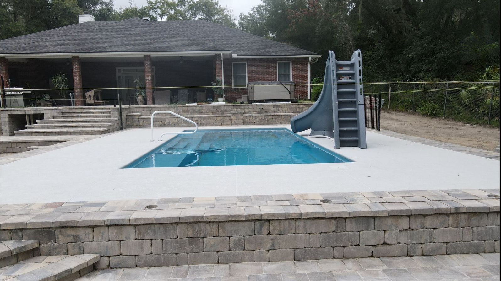 A large swimming pool with a slide in front of a house.