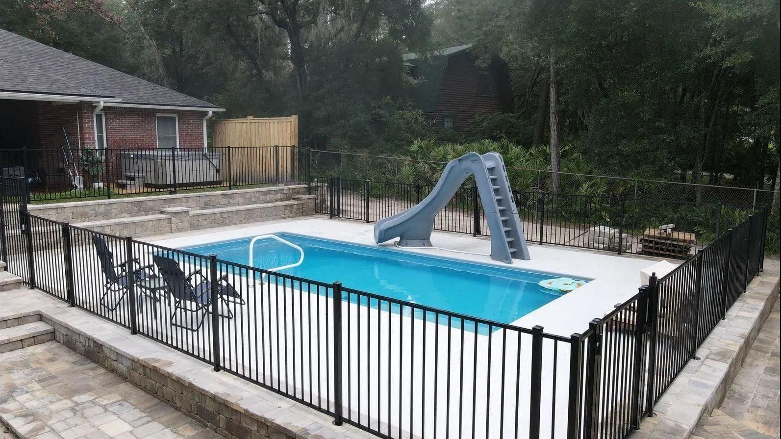 A large swimming pool surrounded by a fence and a slide.