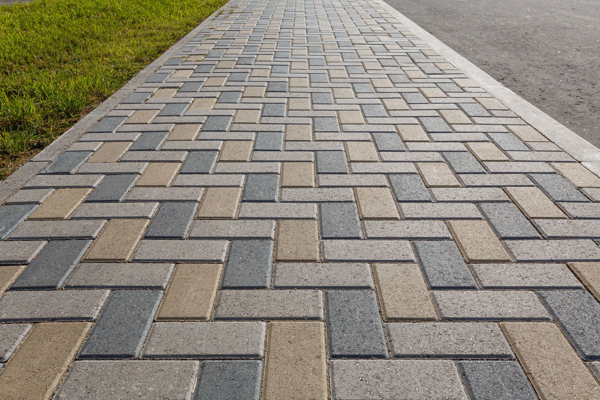 A sidewalk made of bricks is lined with grass.