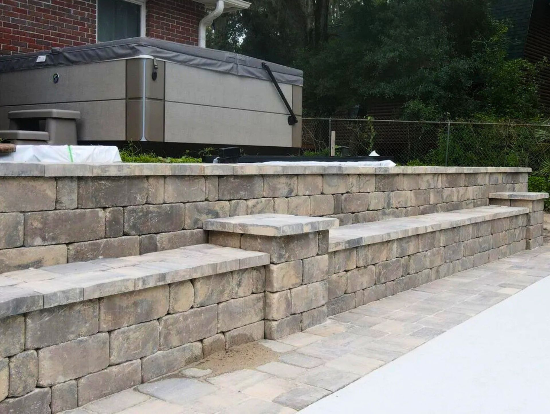 Stone retaining wall with built-in bench seating and steps leading to a raised hot tub beside a bric
